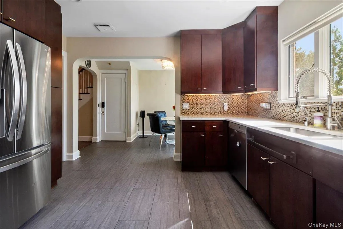 Kitchen with appliances with stainless steel finishes, arched walkways, tasteful backsplash, light countertops, and dark wood-style flooring Kitchen with appliances with stainless steel finishes, arched walkways, tasteful backsplash, light countertops, and dark wood-style flooring