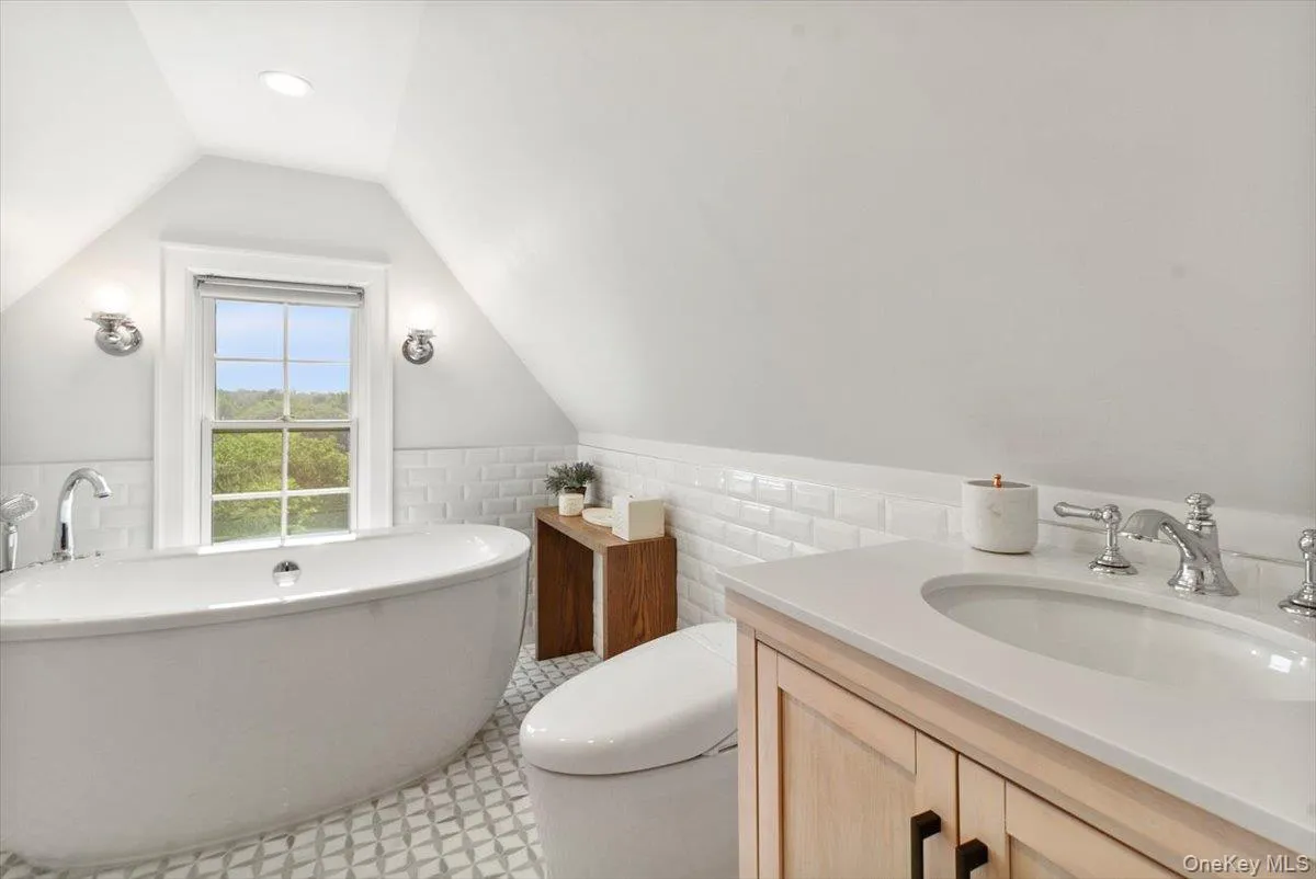 Full bathroom featuring a freestanding bath, vaulted ceiling, wainscoting, vanity, and tile patterned floors Full bathroom featuring a freestanding bath, vaulted ceiling, wainscoting, vanity, and tile patterned floors