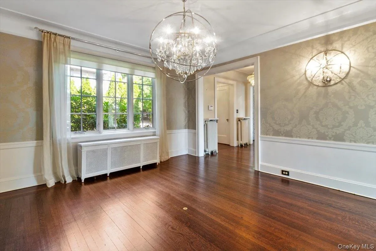 Unfurnished dining area with a chandelier, a wainscoted wall, radiator, wallpapered walls, and hardwood / wood-style floors Unfurnished dining area with a chandelier, a wainscoted wall, radiator, wallpapered walls, and hardwood / wood-style floors