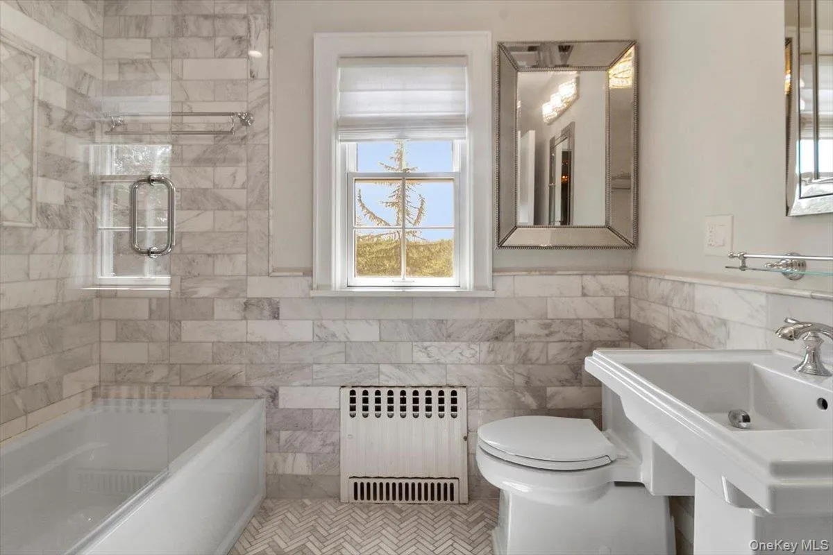 Full bathroom with radiator heating unit, tile walls, shower / bathtub combination, and wainscoting Full bathroom with radiator heating unit, tile walls, shower / bathtub combination, and wainscoting