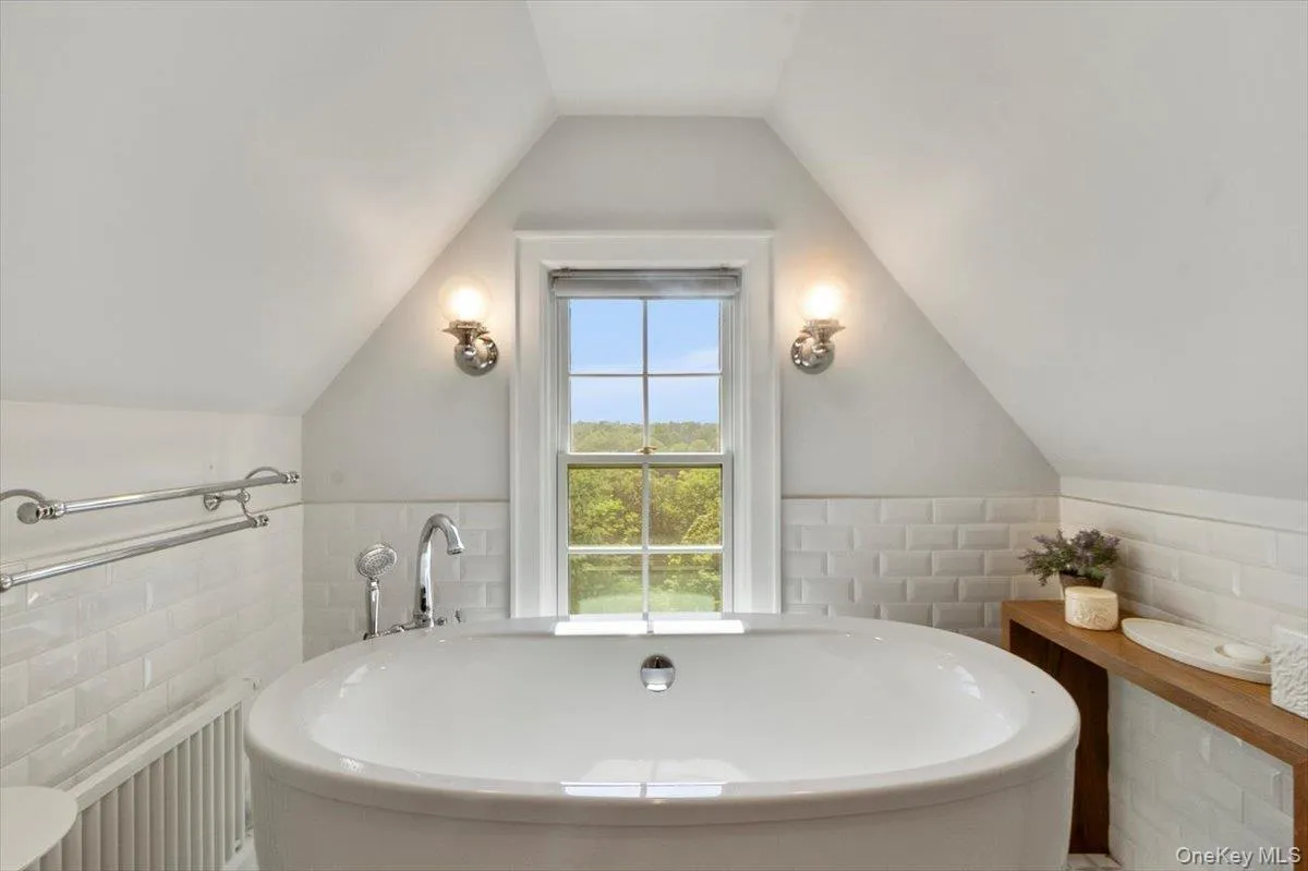 Bathroom featuring a freestanding tub, tile walls, a wainscoted wall, radiator, and lofted ceiling Bathroom featuring a freestanding tub, tile walls, a wainscoted wall, radiator, and lofted ceiling