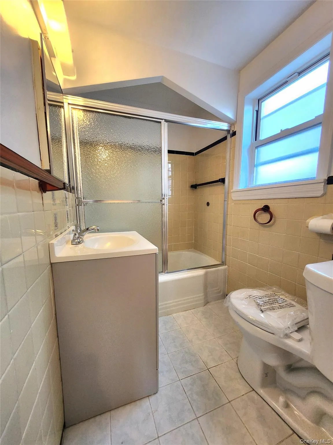 Bathroom featuring tile walls, vanity, light tile patterned flooring, and shower / bath combination with glass door Bathroom featuring tile walls, vanity, light tile patterned flooring, and shower / bath combination with glass door