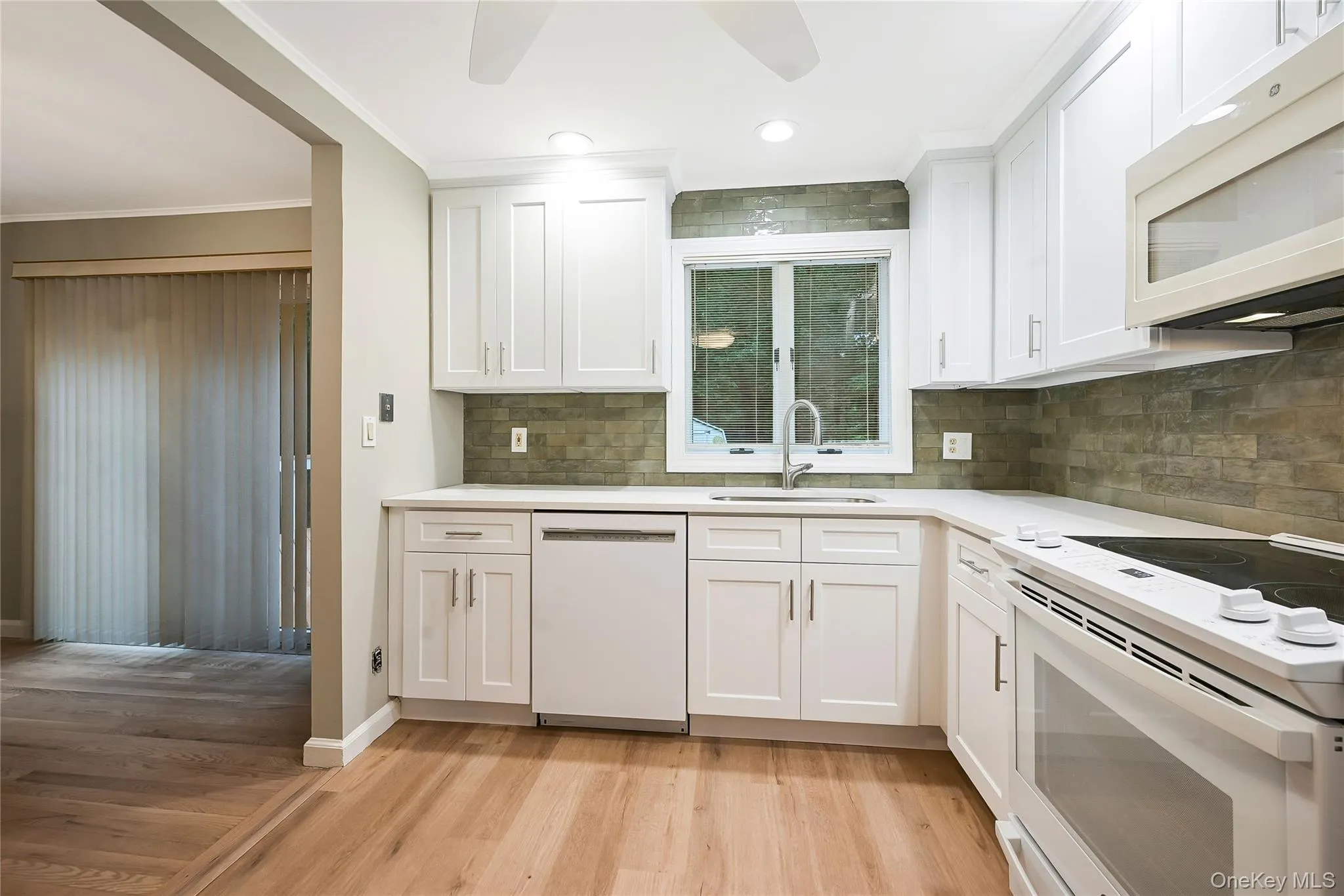 Kitchen featuring white appliances, white cabinets, light wood-style flooring, ornamental molding, and recessed lighting Kitchen featuring white appliances, white cabinets, light wood-style flooring, ornamental molding, and recessed lighting