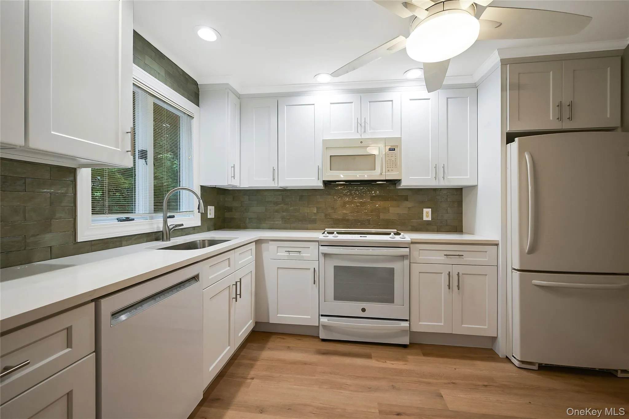 Kitchen featuring white appliances, light wood-style flooring, white cabinetry, decorative backsplash, and a ceiling fan Kitchen featuring white appliances, light wood-style flooring, white cabinetry, decorative backsplash, and a ceiling fan