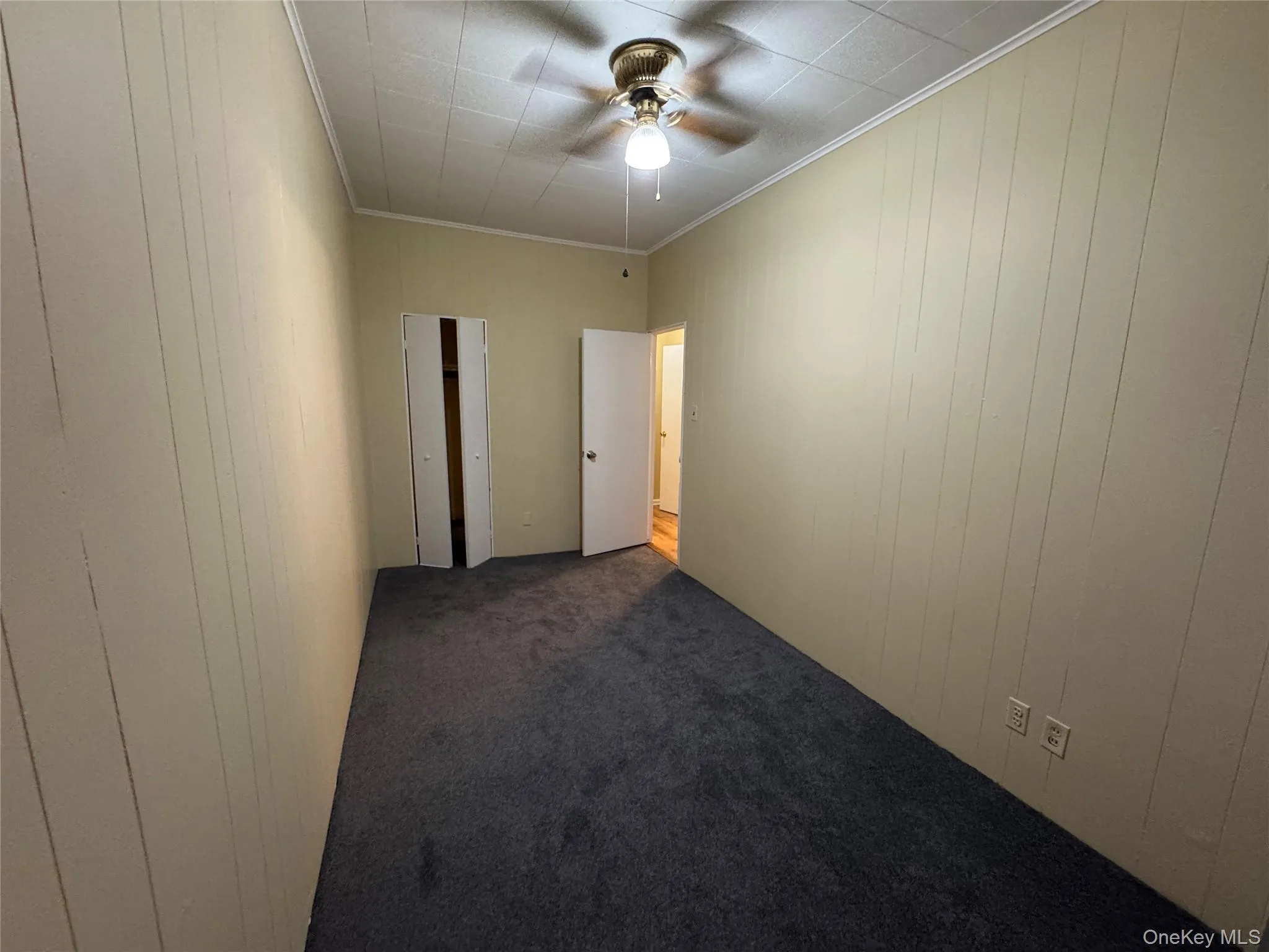 Spare room featuring crown molding, carpet, wooden walls, and a ceiling fan Spare room featuring crown molding, carpet, wooden walls, and a ceiling fan