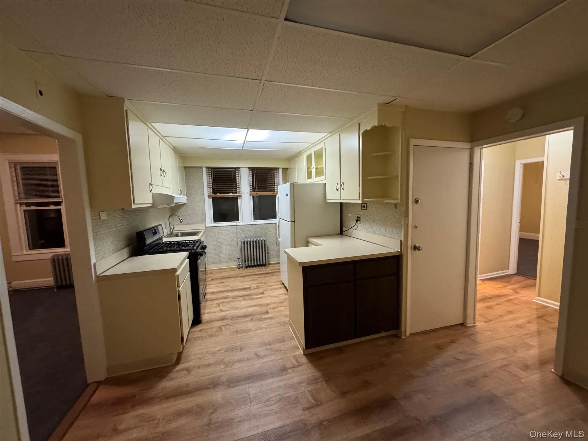 Kitchen featuring a drop ceiling, light countertops, gas stove, white cabinets, and freestanding refrigerator Kitchen featuring a drop ceiling, light countertops, gas stove, white cabinets, and freestanding refrigerator