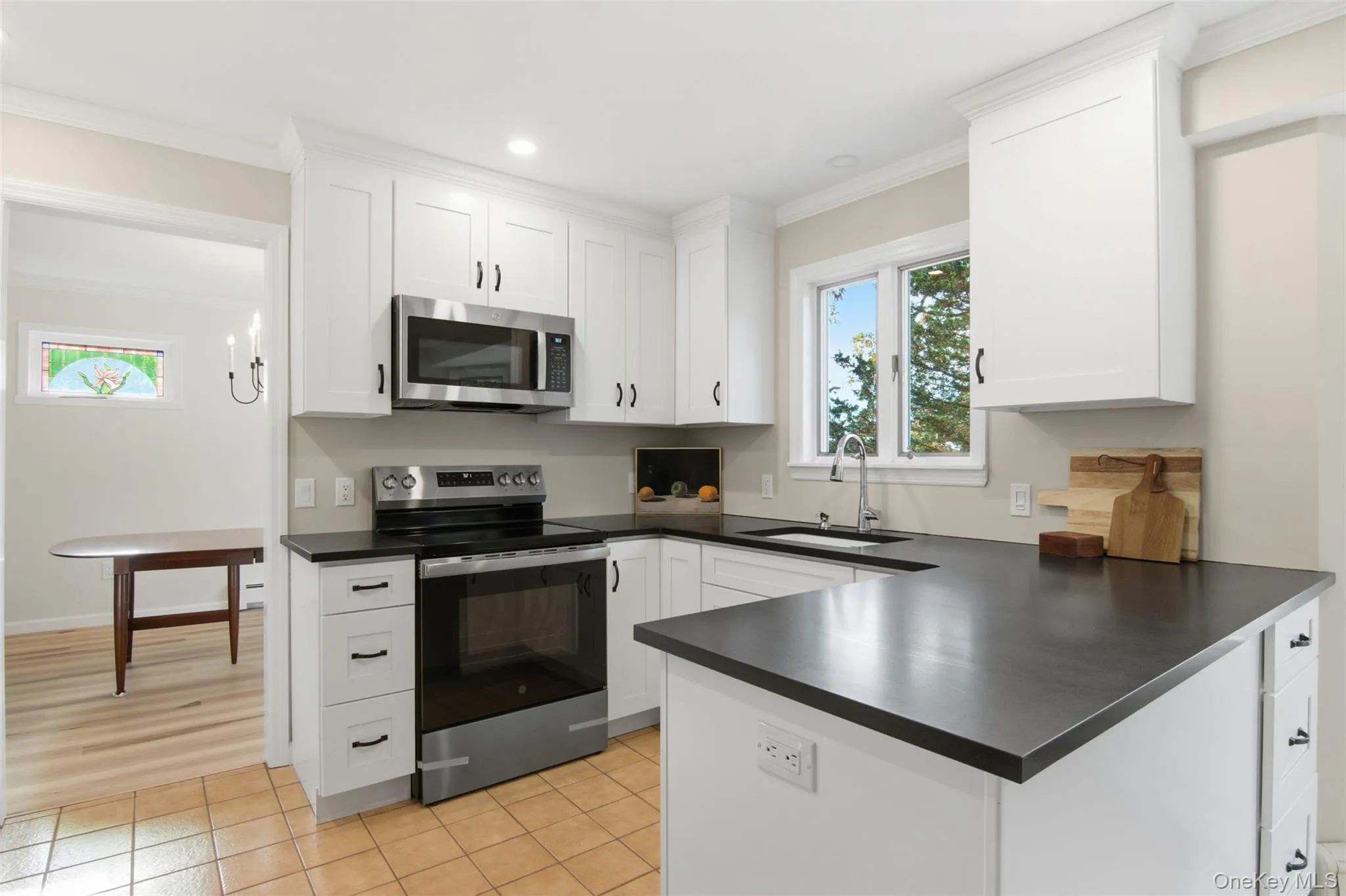 Kitchen featuring stainless steel appliances, crown molding, light tile patterned floors, a peninsula, and white cabinetry Kitchen featuring stainless steel appliances, crown molding, light tile patterned floors, a peninsula, and white cabinetry