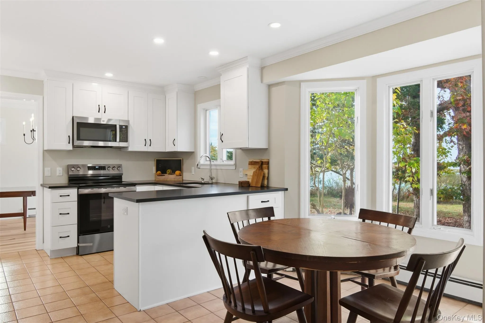 Kitchen featuring appliances with stainless steel finishes, crown molding, light tile patterned floors, dark countertops, and a peninsula Kitchen featuring appliances with stainless steel finishes, crown molding, light tile patterned floors, dark countertops, and a peninsula