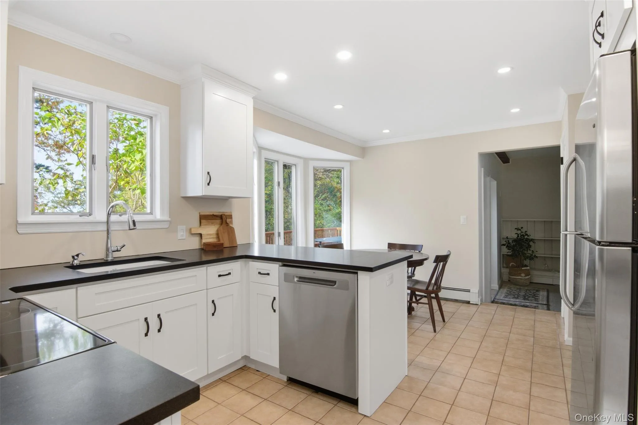 Kitchen with a peninsula, dark countertops, stainless steel appliances, crown molding, and white cabinetry Kitchen with a peninsula, dark countertops, stainless steel appliances, crown molding, and white cabinetry
