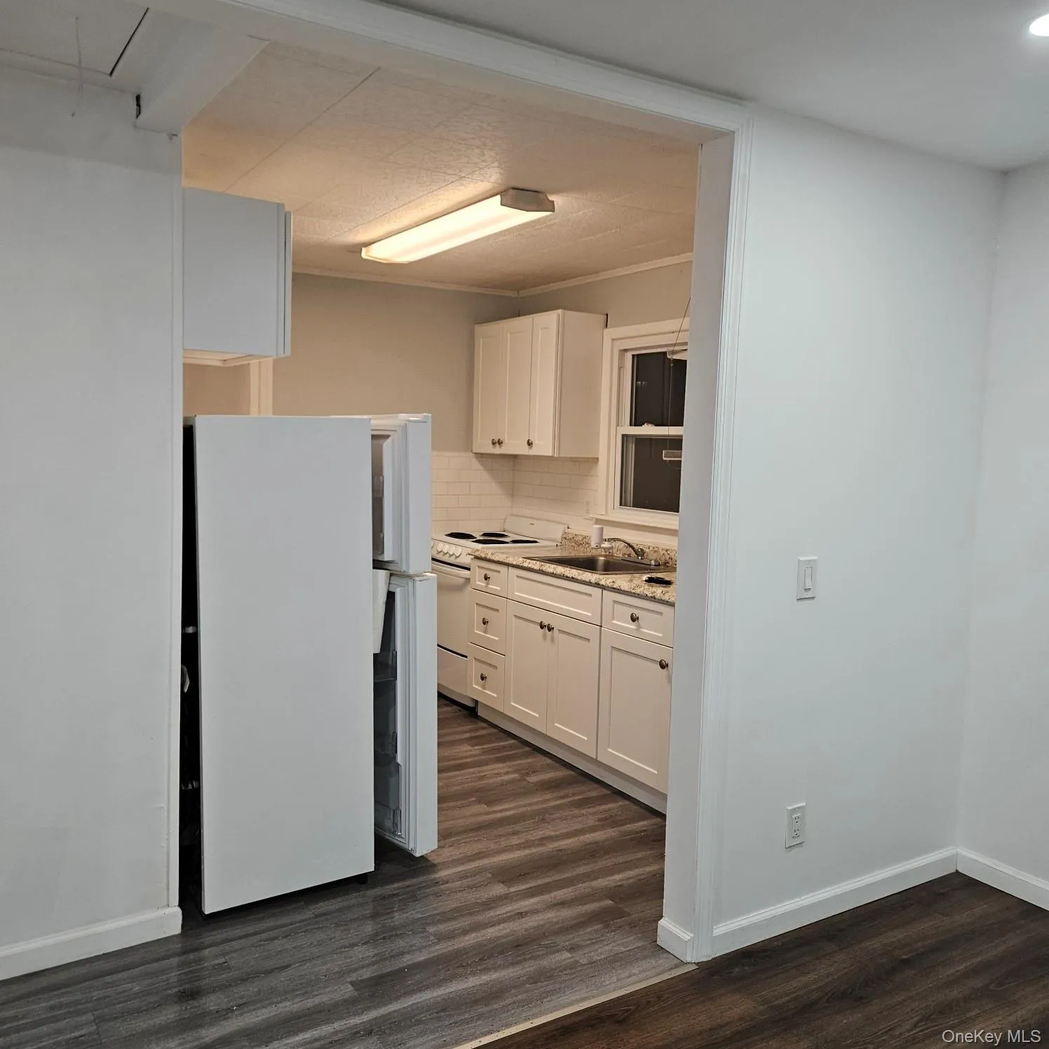 Kitchen with white cabinets, white appliances, dark wood-style flooring, tasteful backsplash, and ornamental molding Kitchen with white cabinets, white appliances, dark wood-style flooring, tasteful backsplash, and ornamental molding