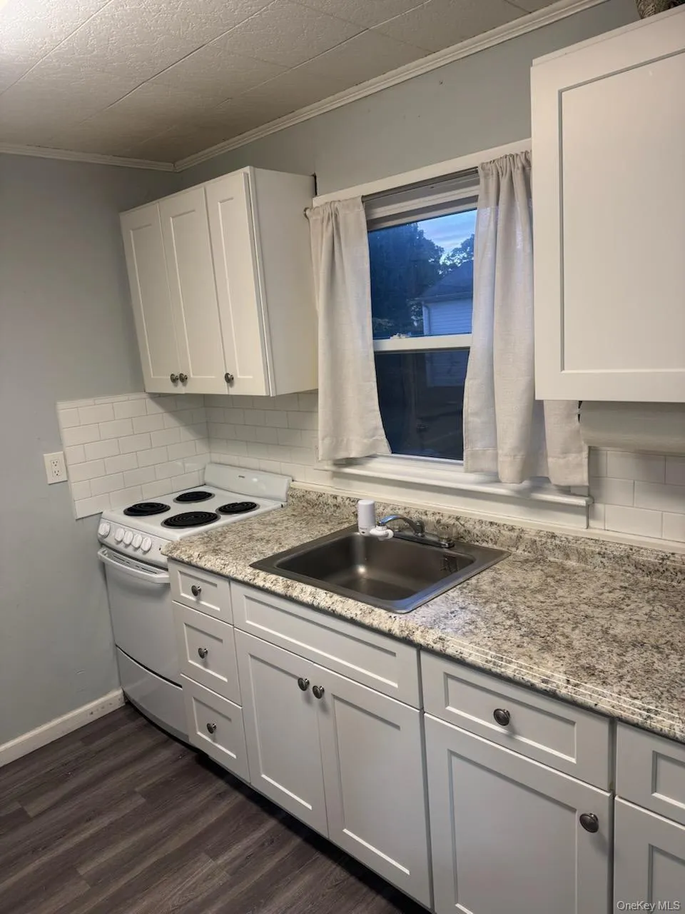 Kitchen featuring electric stove, white cabinetry, backsplash, dark wood finished floors, and ornamental molding Kitchen featuring electric stove, white cabinetry, backsplash, dark wood finished floors, and ornamental molding