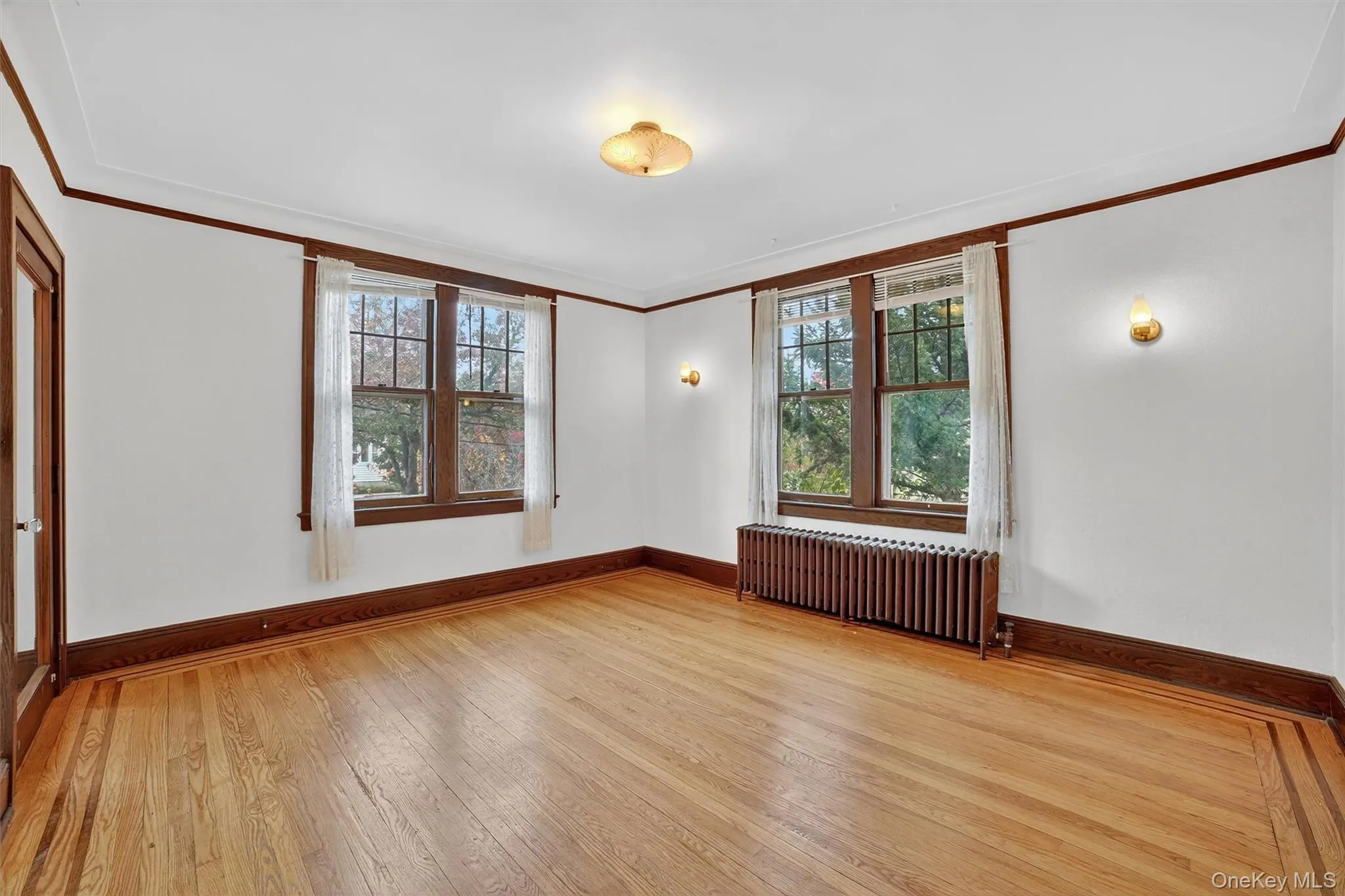Spare room with crown molding, healthy amount of natural light, light wood-style flooring, and radiator Spare room with crown molding, healthy amount of natural light, light wood-style flooring, and radiator