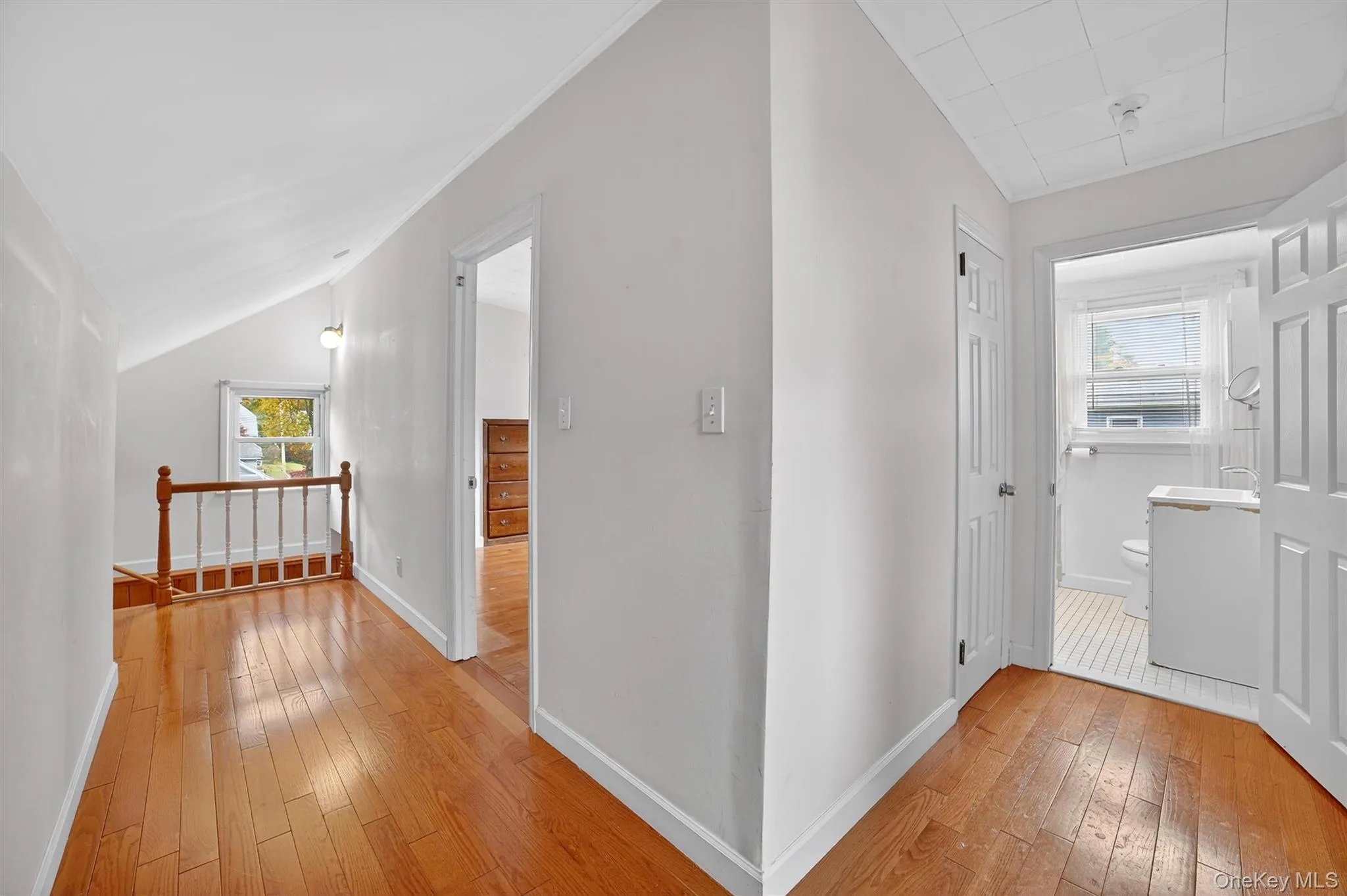 Hallway featuring light wood finished floors, healthy amount of natural light, an upstairs landing, and vaulted ceiling Hallway featuring light wood finished floors, healthy amount of natural light, an upstairs landing, and vaulted ceiling