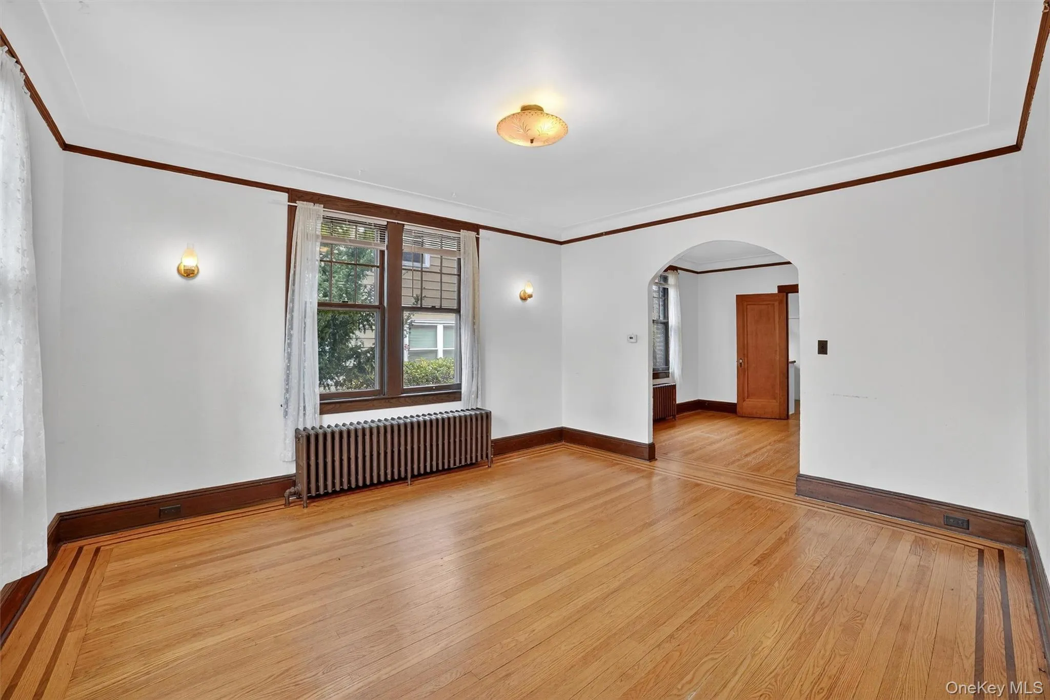 Empty room featuring ornamental molding, arched walkways, light wood-type flooring, and radiator heating unit Empty room featuring ornamental molding, arched walkways, light wood-type flooring, and radiator heating unit