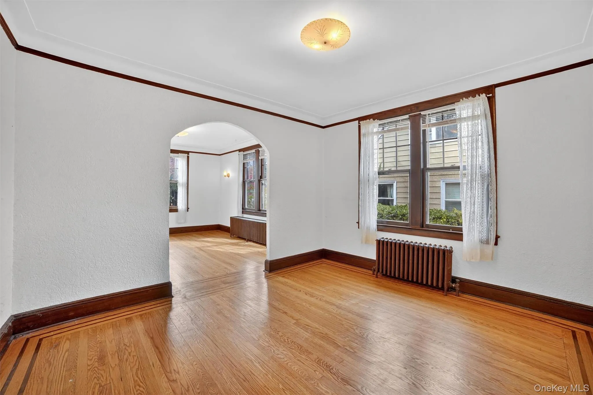 Unfurnished room featuring crown molding, plenty of natural light, light wood-style floors, a textured wall, and radiator Unfurnished room featuring crown molding, plenty of natural light, light wood-style floors, a textured wall, and radiator