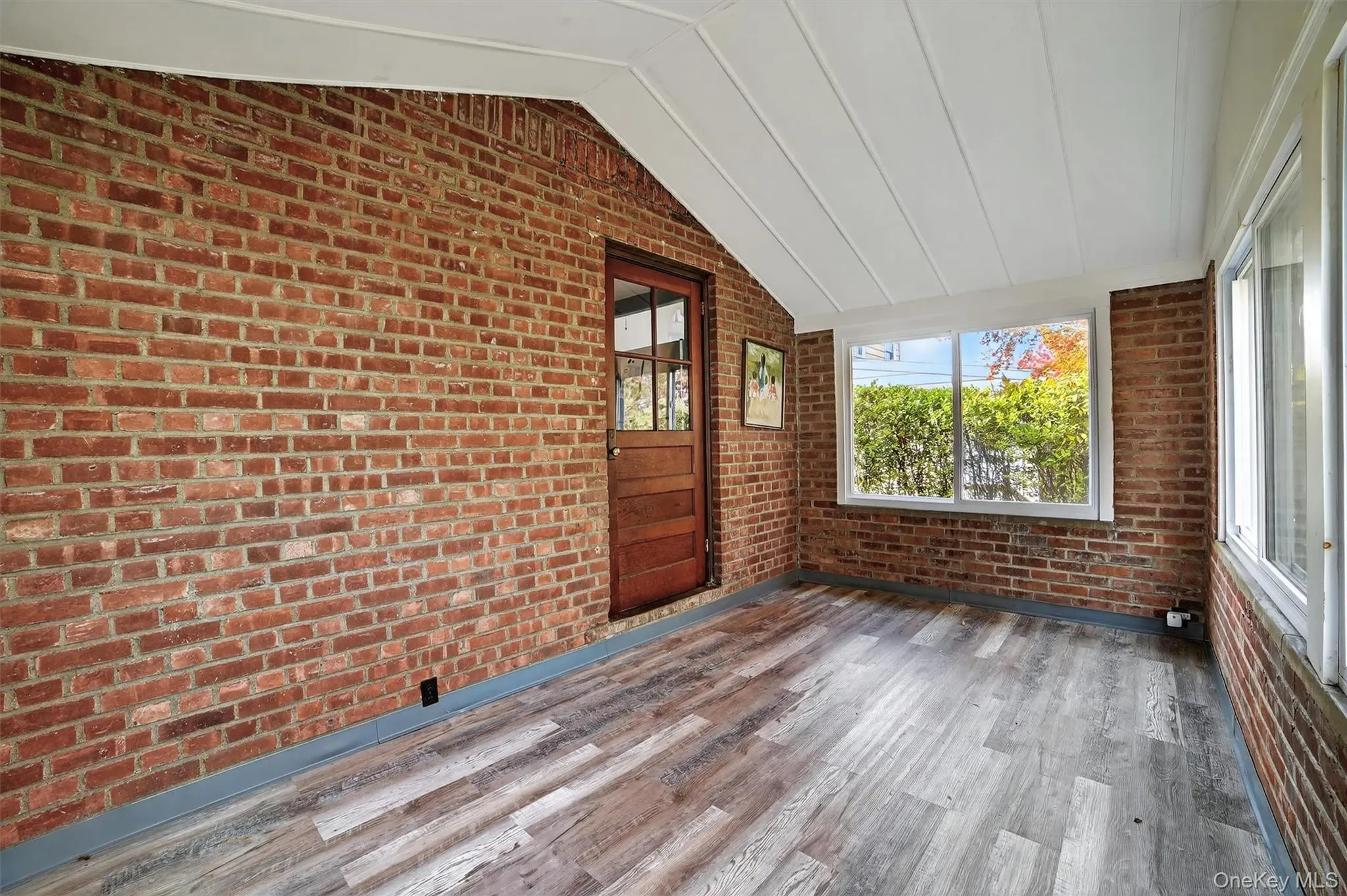 Unfurnished sunroom with vaulted ceiling, brick wall, and wood finished floors Unfurnished sunroom with vaulted ceiling, brick wall, and wood finished floors