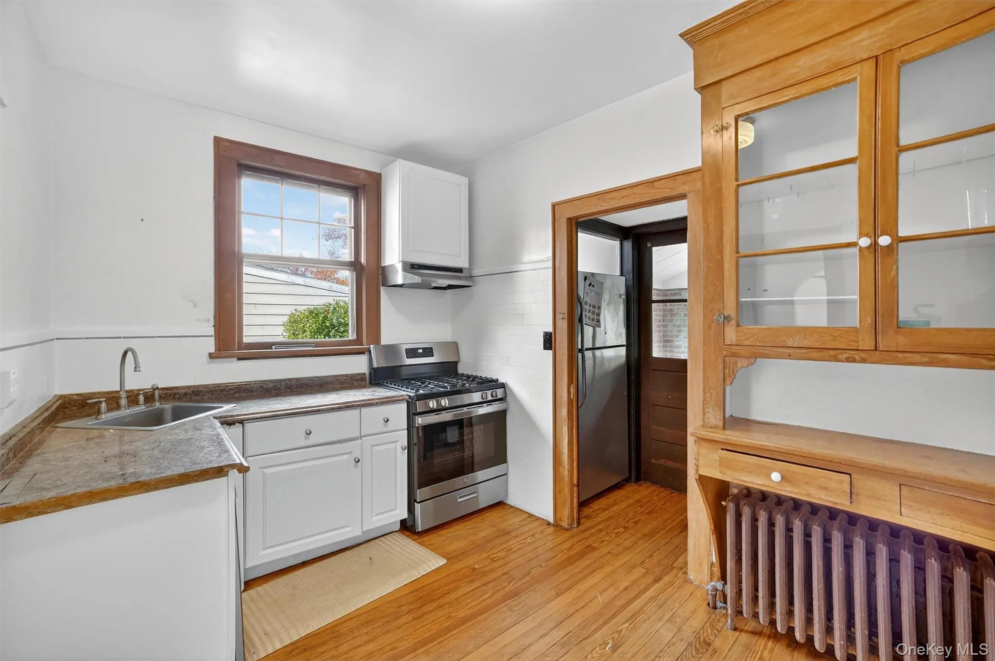 Kitchen with white cabinets, radiator heating unit, appliances with stainless steel finishes, and light wood-style floors Kitchen with white cabinets, radiator heating unit, appliances with stainless steel finishes, and light wood-style floors