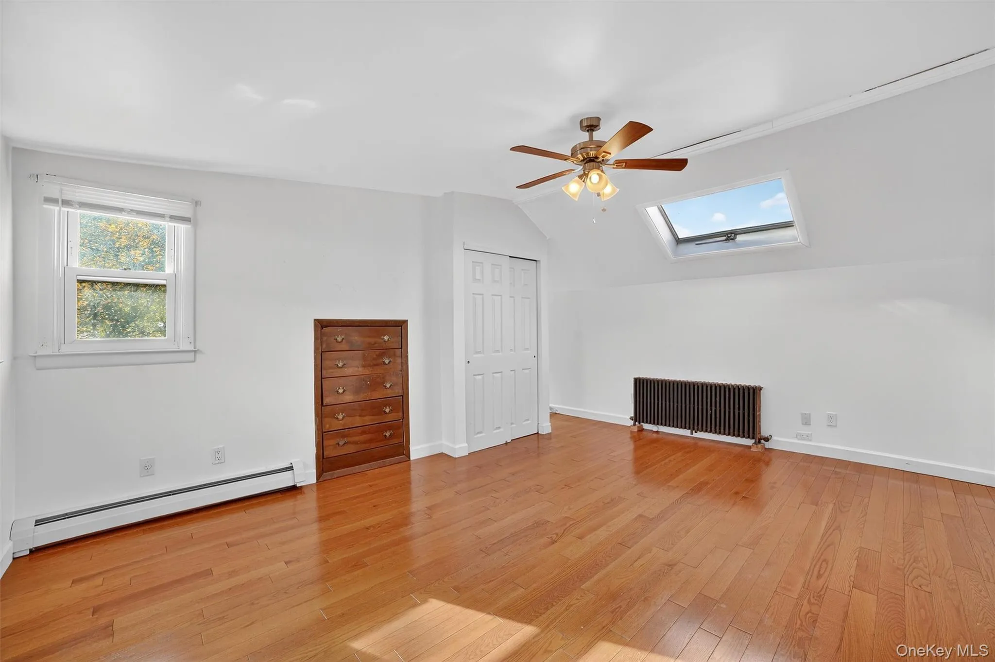 Additional living space featuring a skylight, a baseboard radiator, radiator, vaulted ceiling, and light wood finished floors Additional living space featuring a skylight, a baseboard radiator, radiator, vaulted ceiling, and light wood finished floors