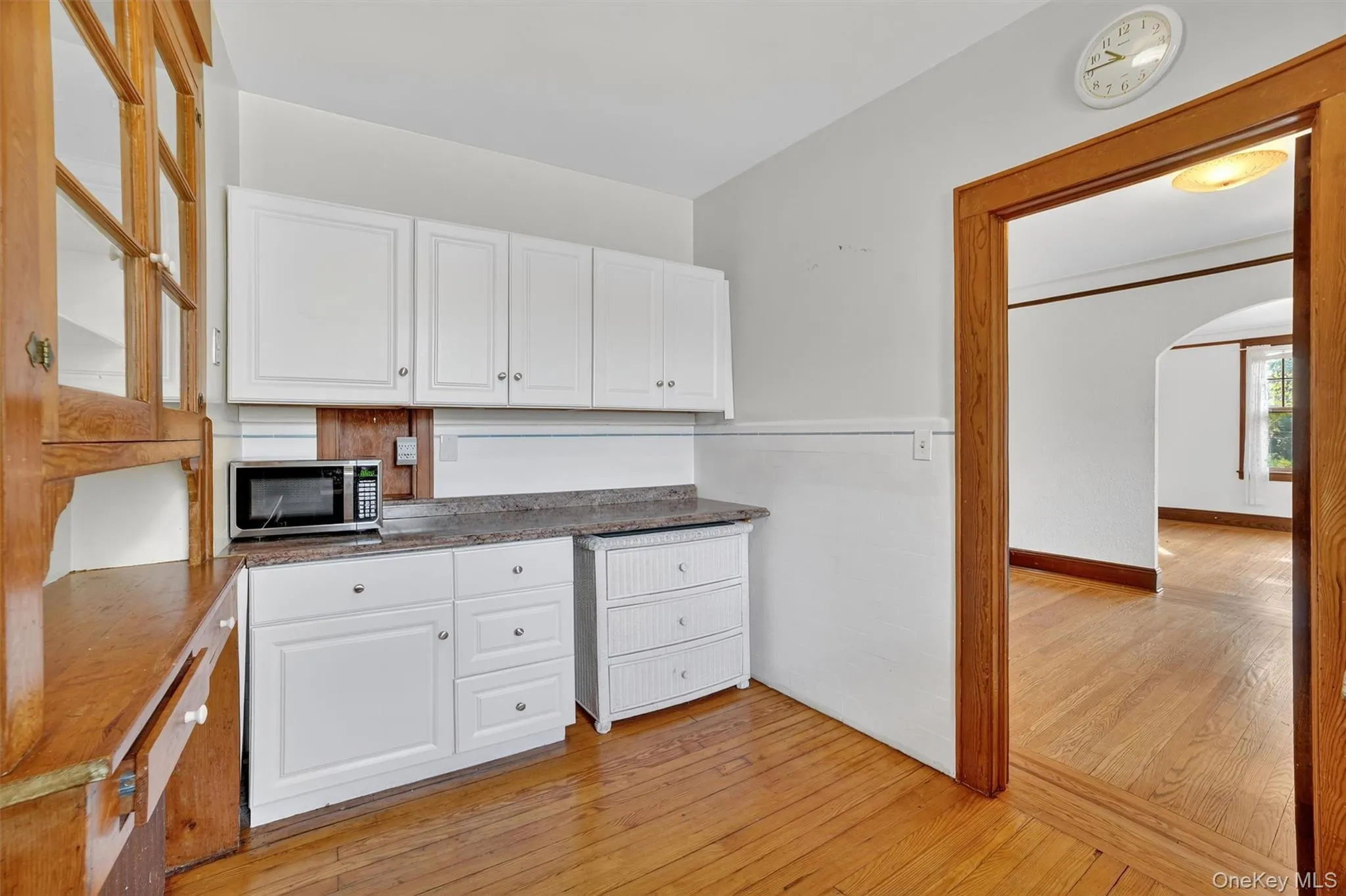 Kitchen with light wood finished floors, white cabinetry, arched walkways, and stainless steel microwave Kitchen with light wood finished floors, white cabinetry, arched walkways, and stainless steel microwave