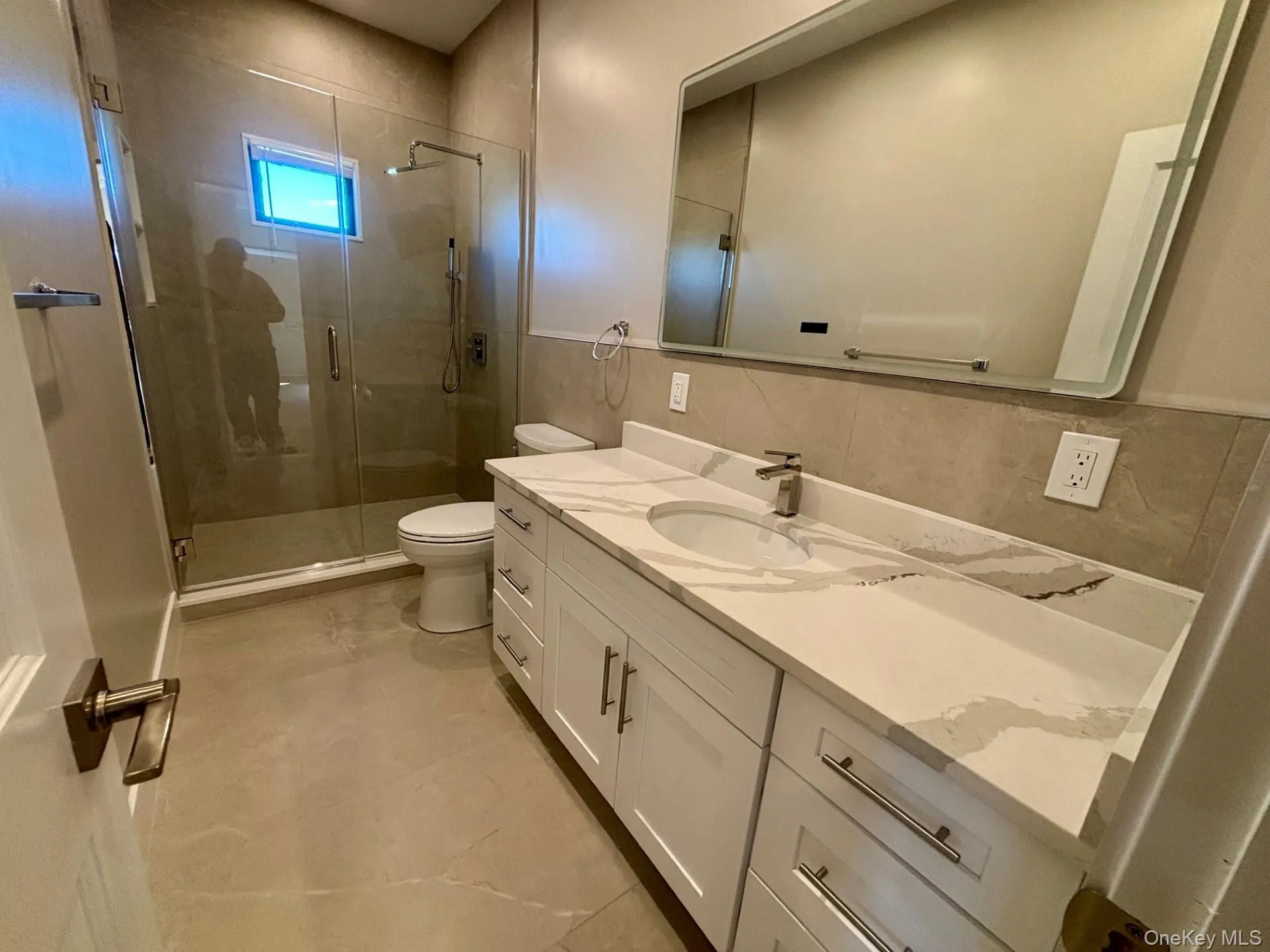 Full bathroom with vanity, a stall shower, tile walls, a wainscoted wall, and light tile patterned floors Full bathroom with vanity, a stall shower, tile walls, a wainscoted wall, and light tile patterned floors