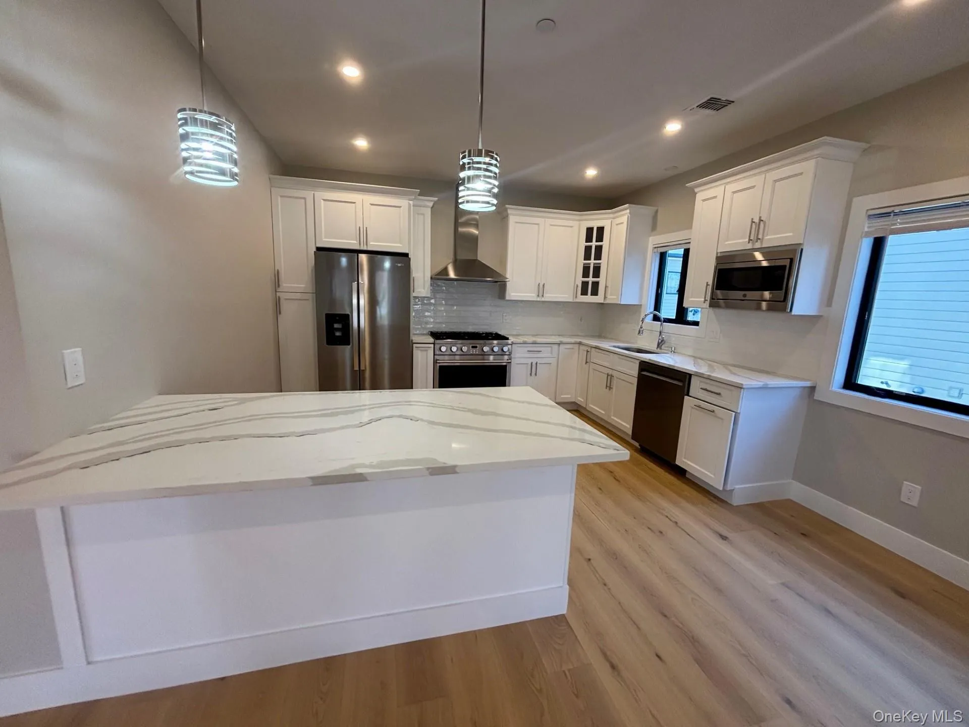 Kitchen featuring glass insert cabinets, white cabinets, appliances with stainless steel finishes, tasteful backsplash, and recessed lighting Kitchen featuring glass insert cabinets, white cabinets, appliances with stainless steel finishes, tasteful backsplash, and recessed lighting