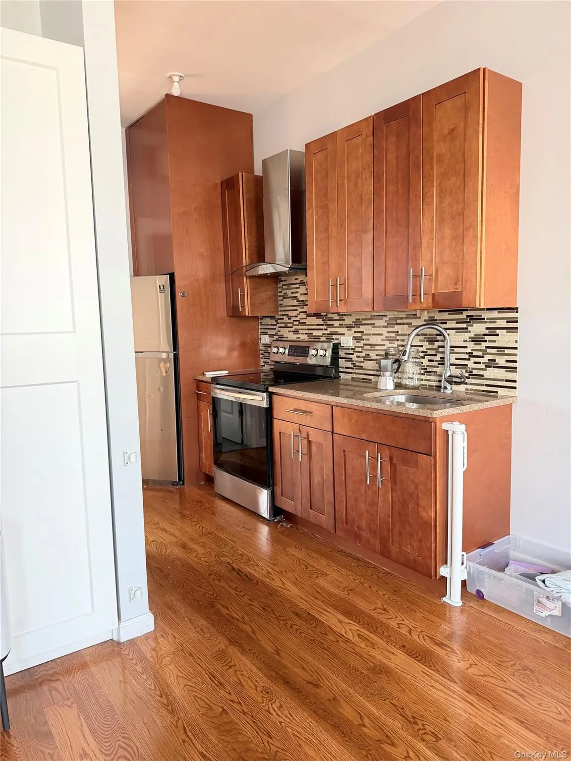 Kitchen with brown cabinetry, stainless steel appliances, wall chimney exhaust hood, and backsplash Kitchen with brown cabinetry, stainless steel appliances, wall chimney exhaust hood, and backsplash