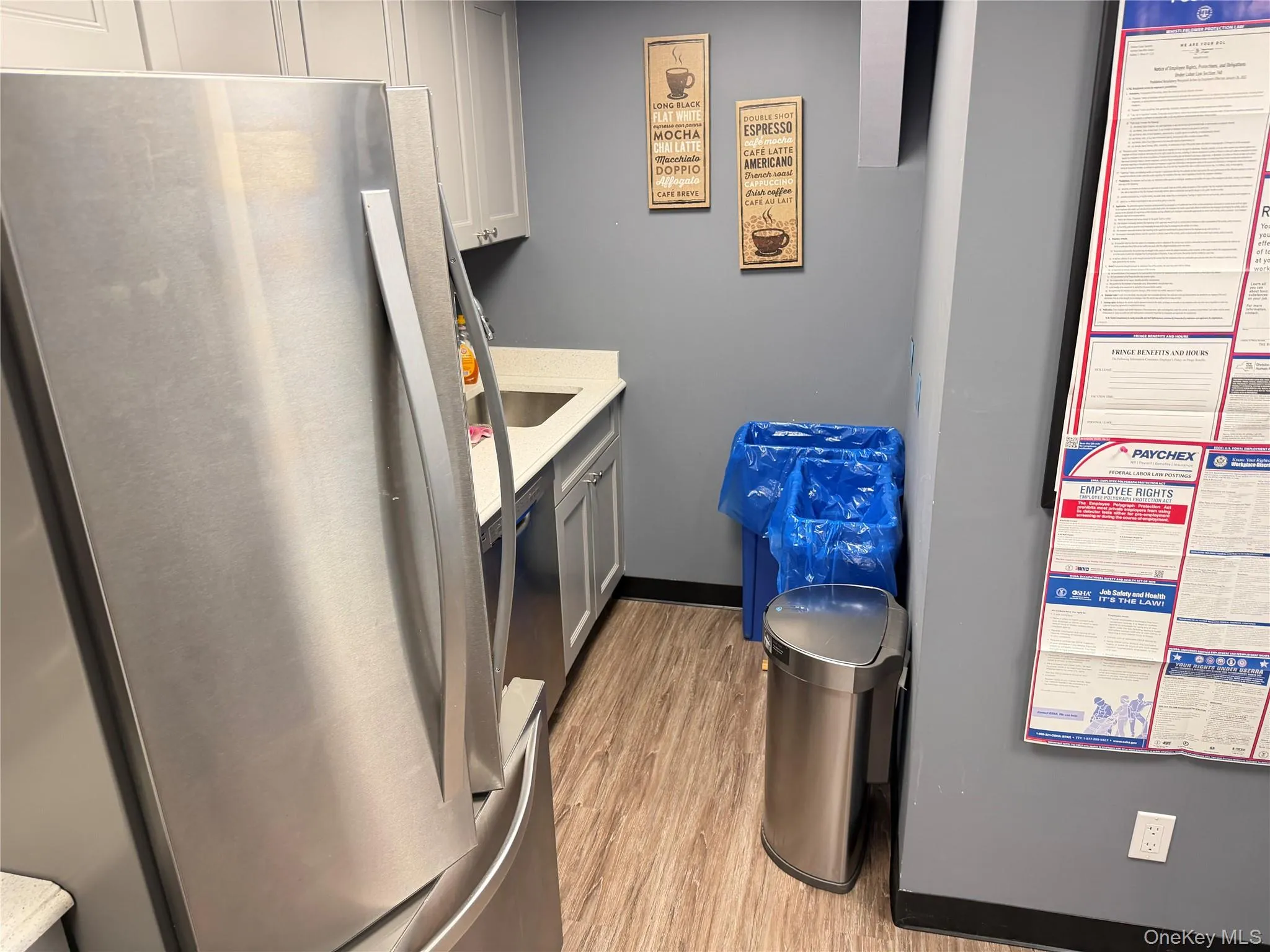 Kitchen with appliances with stainless steel finishes, light wood-style flooring, a heating unit, light stone countertops, and gray cabinetry Kitchen with appliances with stainless steel finishes, light wood-style flooring, a heating unit, light stone countertops, and gray cabinetry