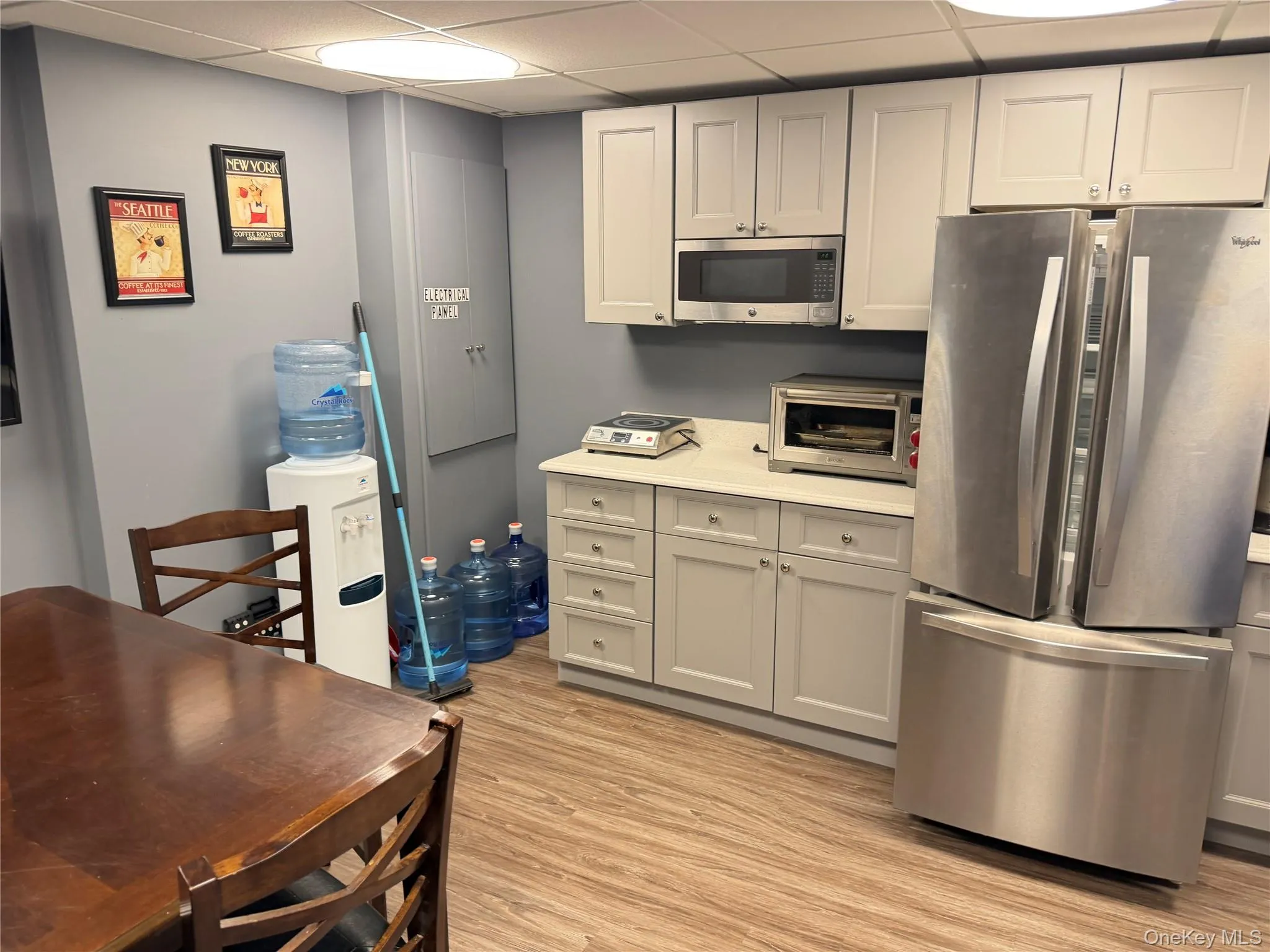 Kitchen with stainless steel appliances, a paneled ceiling, light countertops, light wood-style floors, and white cabinetry Kitchen with stainless steel appliances, a paneled ceiling, light countertops, light wood-style floors, and white cabinetry