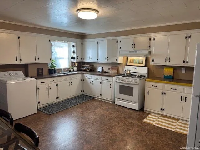 Kitchen with washer / clothes dryer, white appliances, ornamental molding, white cabinetry, and dark countertops Kitchen with washer / clothes dryer, white appliances, ornamental molding, white cabinetry, and dark countertops