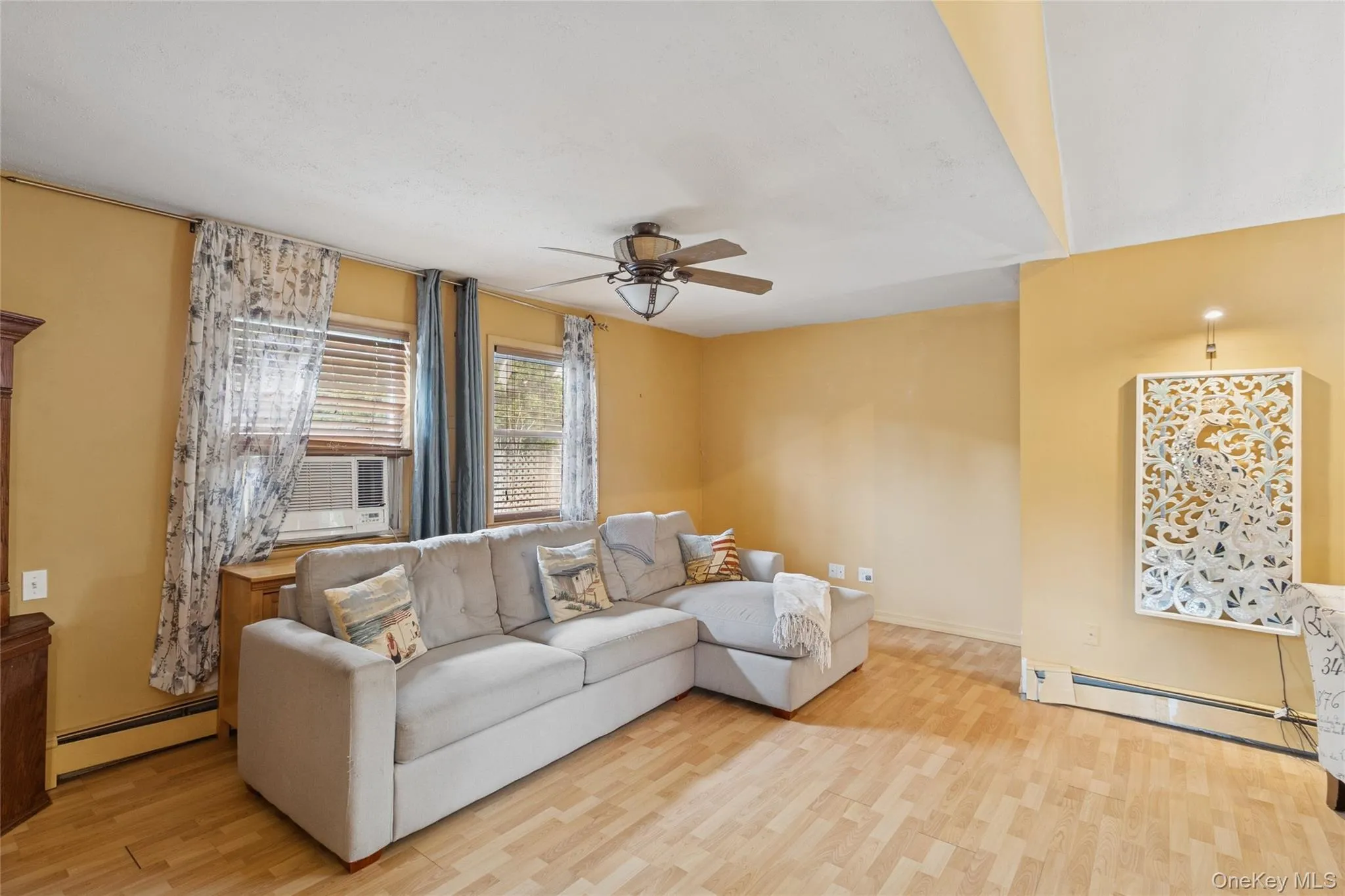 Living room with baseboard heating, light wood finished floors, ceiling fan, and cooling unit Living room with baseboard heating, light wood finished floors, ceiling fan, and cooling unit