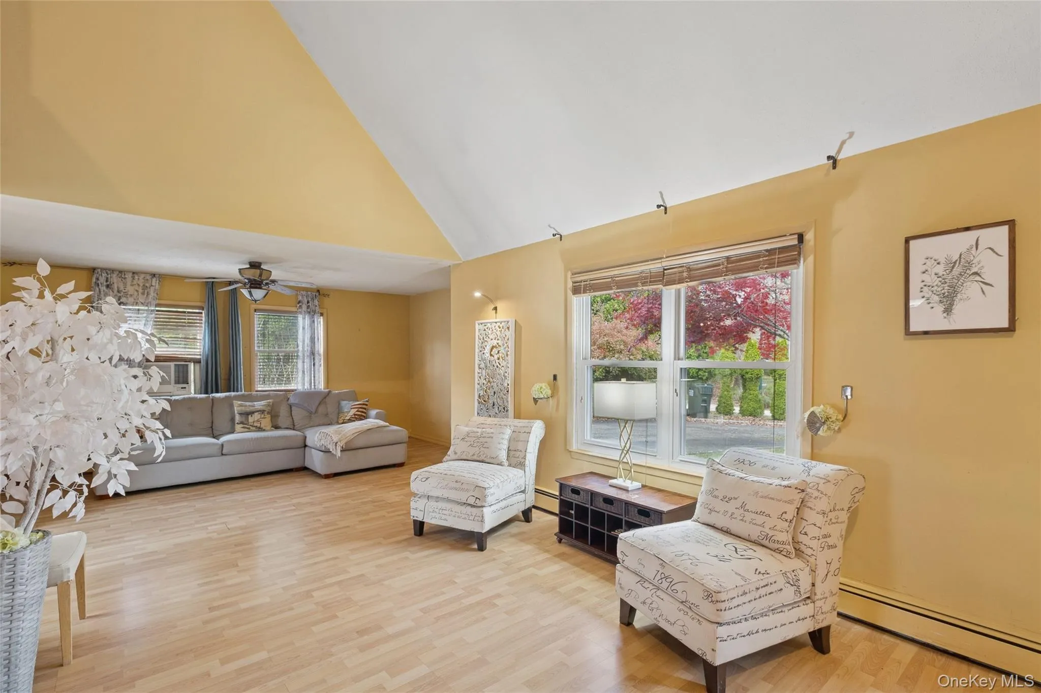Living room featuring a baseboard radiator, high vaulted ceiling, light wood-type flooring, healthy amount of natural light, and ceiling fan Living room featuring a baseboard radiator, high vaulted ceiling, light wood-type flooring, healthy amount of natural light, and ceiling fan
