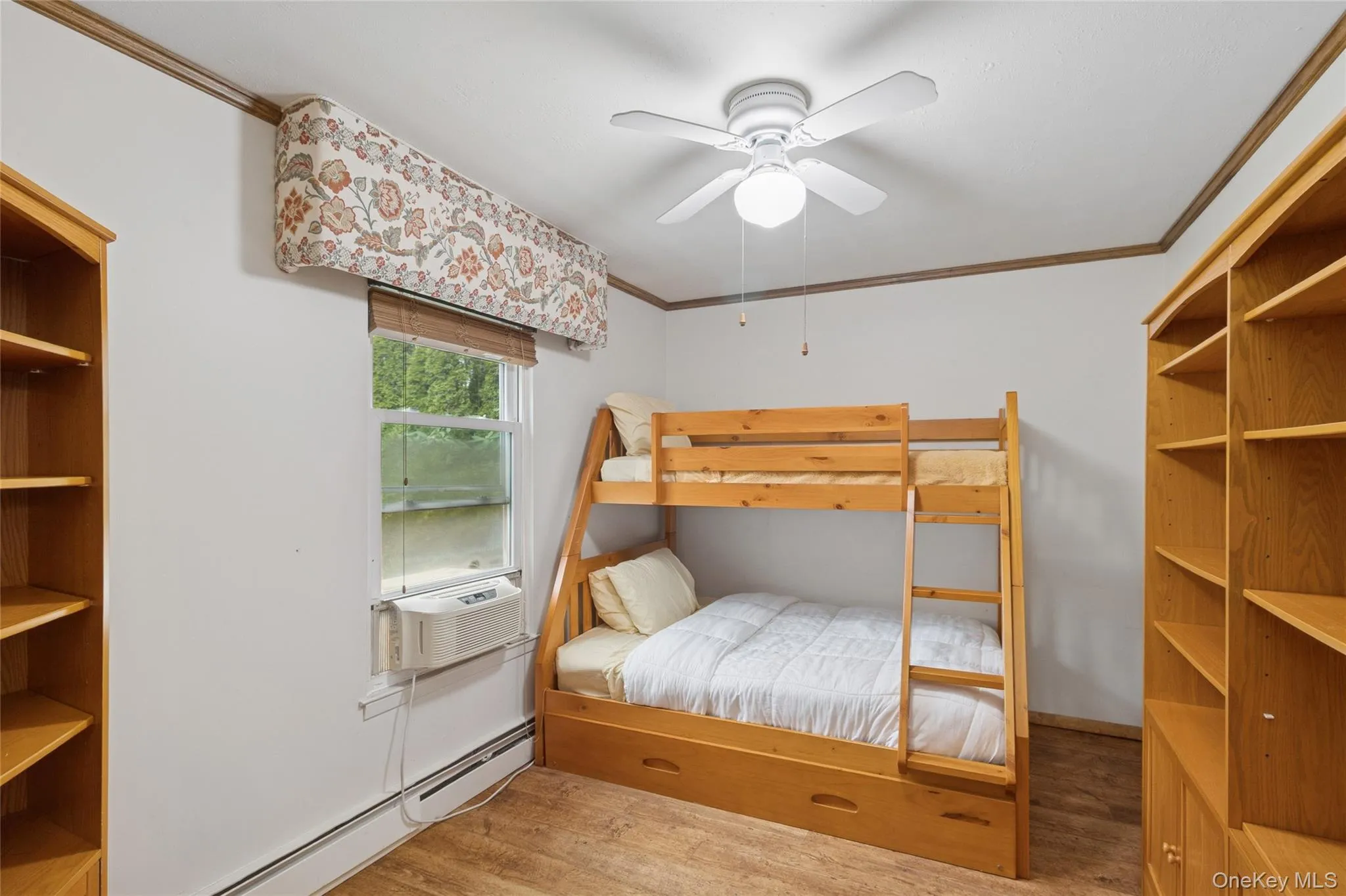 Bedroom with ornamental molding, baseboard heating, light wood finished floors, a ceiling fan, and cooling unit Bedroom with ornamental molding, baseboard heating, light wood finished floors, a ceiling fan, and cooling unit