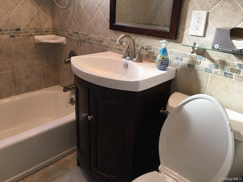 Full bath featuring decorative backsplash, vanity, tile walls, tile patterned floors, and bathing tub / shower combination Full bath featuring decorative backsplash, vanity, tile walls, tile patterned floors, and bathing tub / shower combination