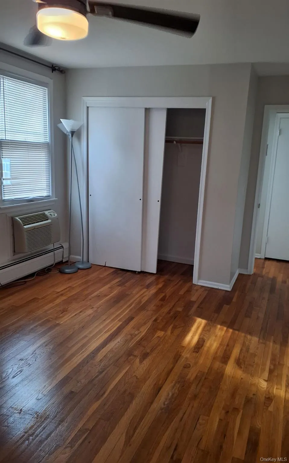 Unfurnished bedroom with wood-type flooring, a ceiling fan, baseboard heating, and a closet Unfurnished bedroom with wood-type flooring, a ceiling fan, baseboard heating, and a closet