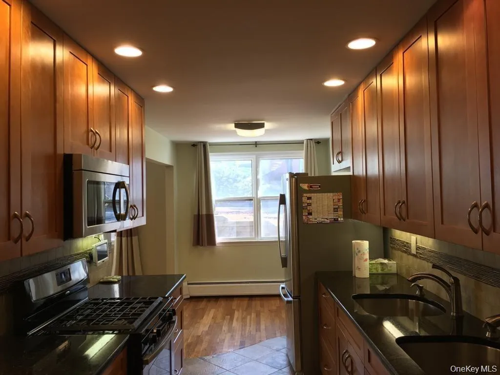 Kitchen with stainless steel appliances, backsplash, dark stone counters, brown cabinetry, and recessed lighting Kitchen with stainless steel appliances, backsplash, dark stone counters, brown cabinetry, and recessed lighting