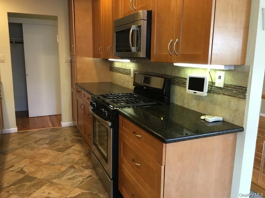 Kitchen with appliances with stainless steel finishes, dark stone countertops, tasteful backsplash, and brown cabinetry Kitchen with appliances with stainless steel finishes, dark stone countertops, tasteful backsplash, and brown cabinetry