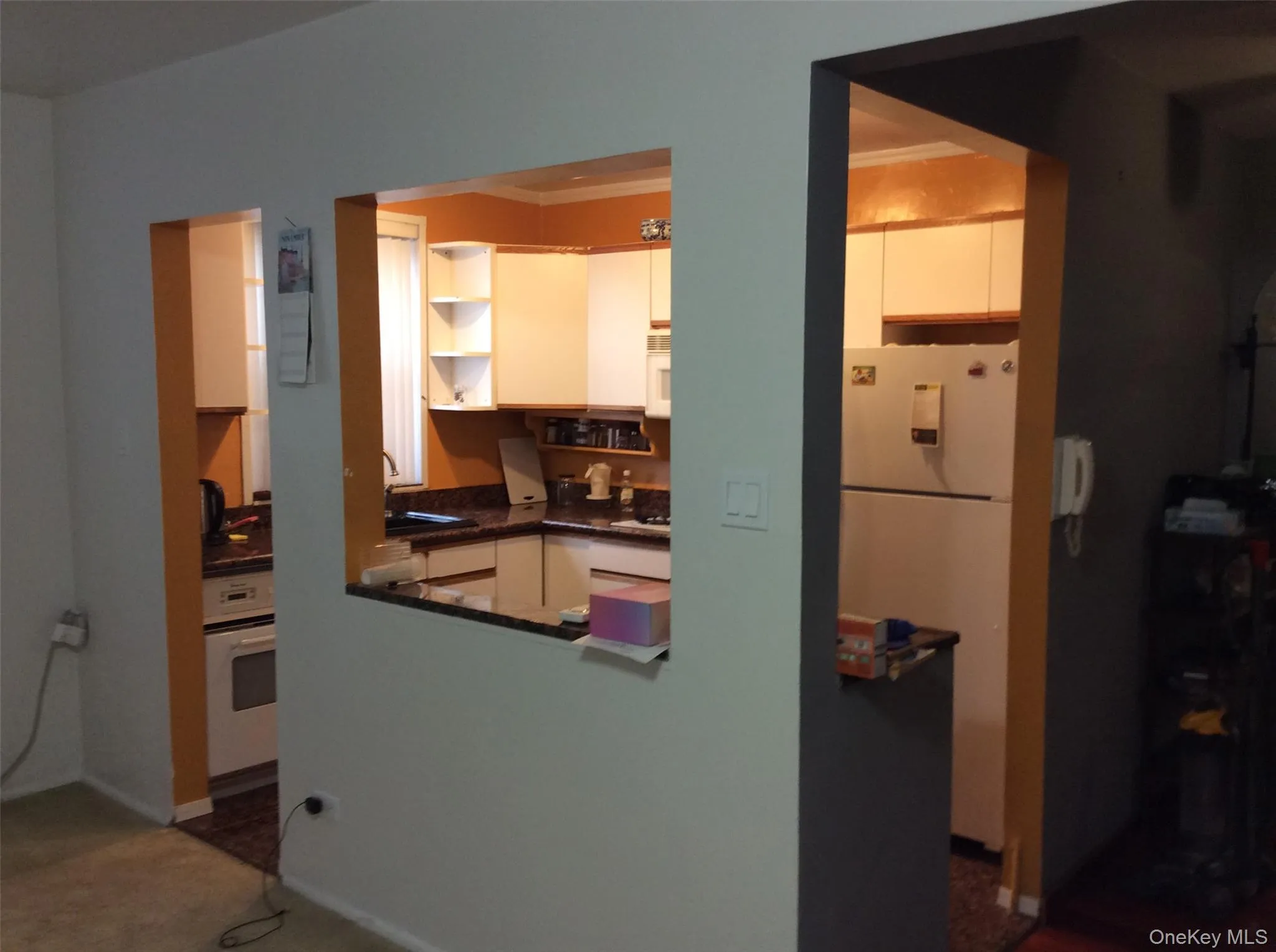 Kitchen featuring white appliances, open shelves, ornamental molding, and dark colored carpet Kitchen featuring white appliances, open shelves, ornamental molding, and dark colored carpet