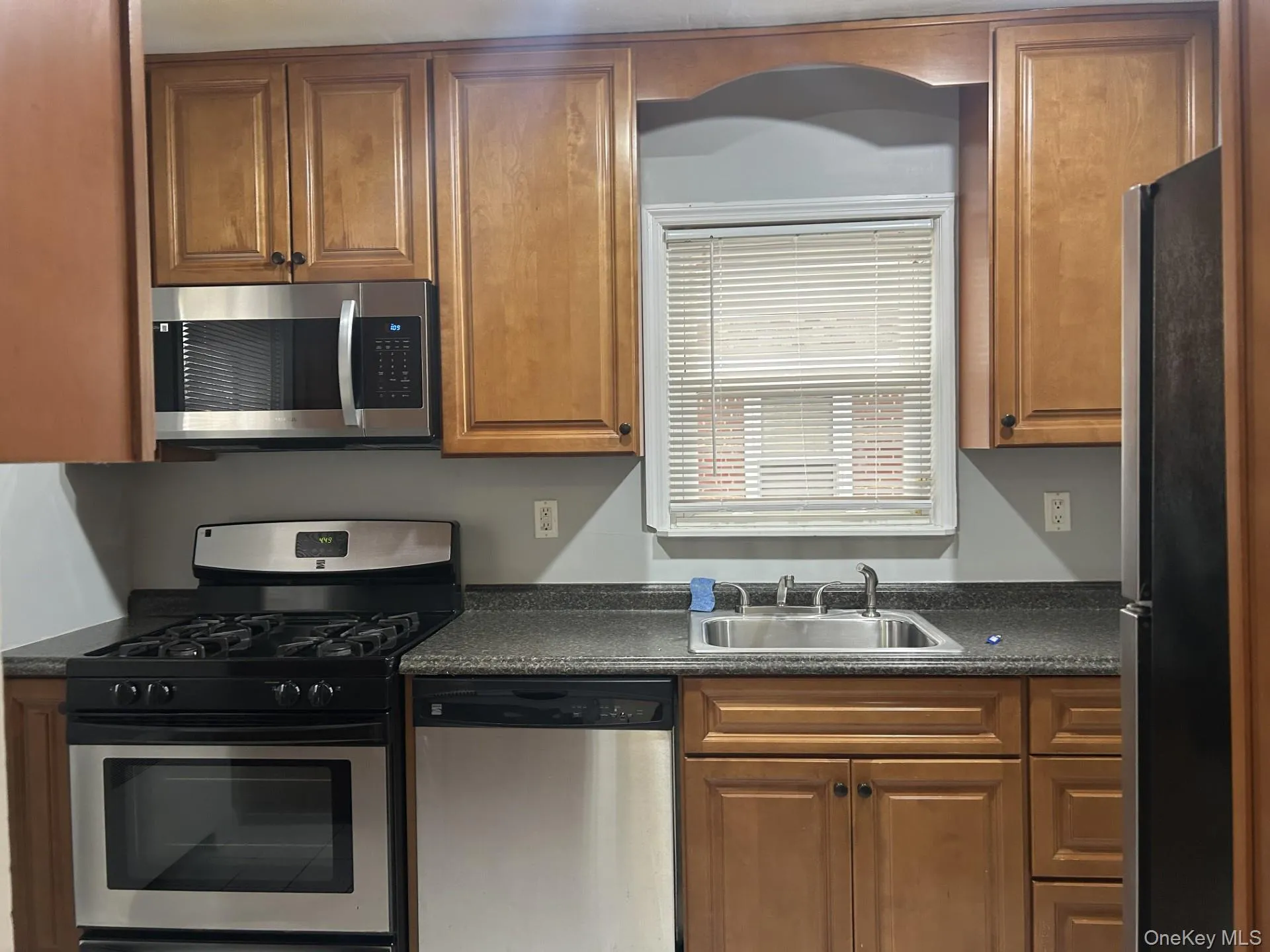Kitchen featuring appliances with stainless steel finishes, dark countertops, and brown cabinets Kitchen featuring appliances with stainless steel finishes, dark countertops, and brown cabinets