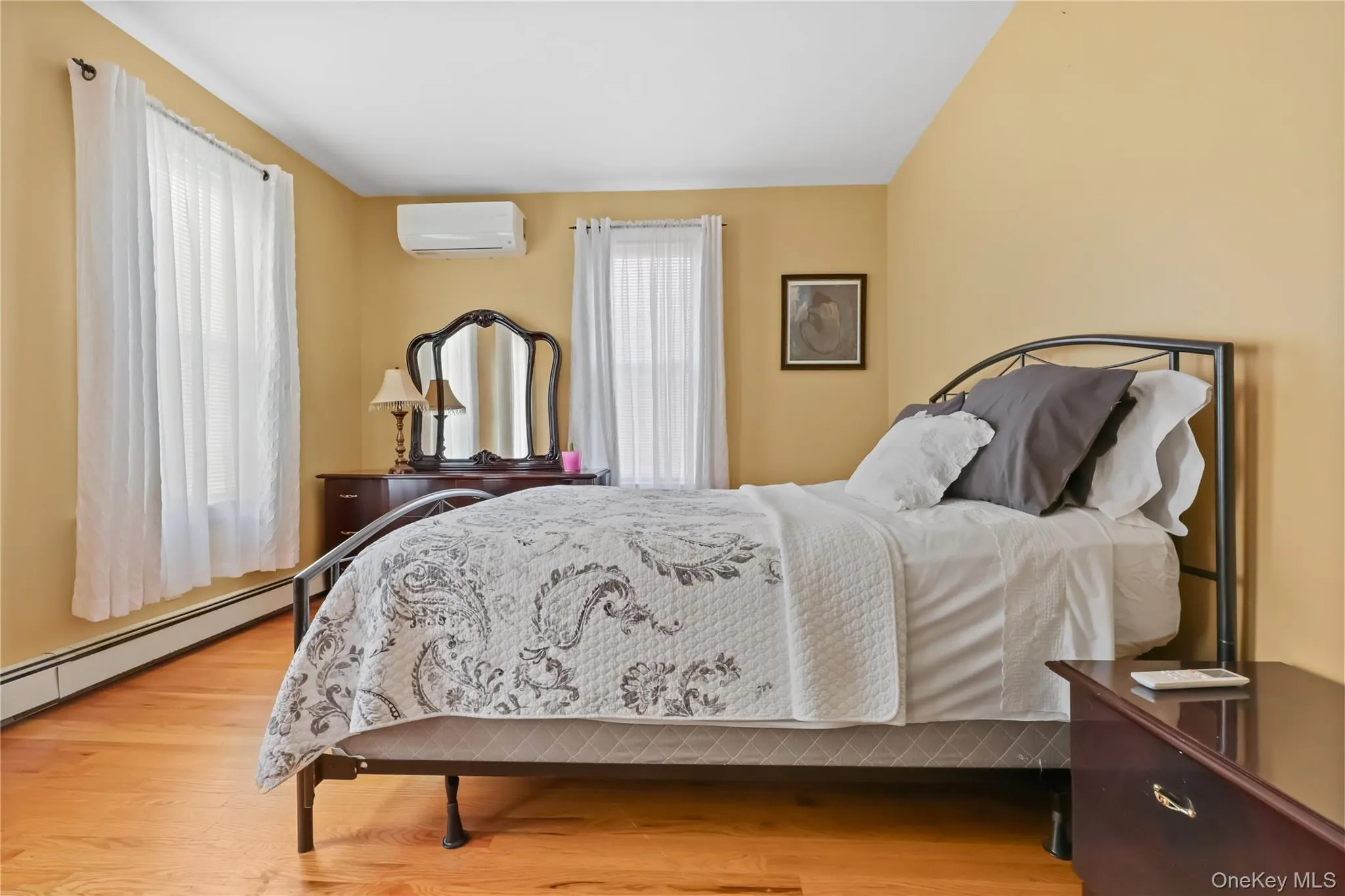Bedroom featuring light wood-style floors, a baseboard radiator, and a wall mounted AC Bedroom featuring light wood-style floors, a baseboard radiator, and a wall mounted AC