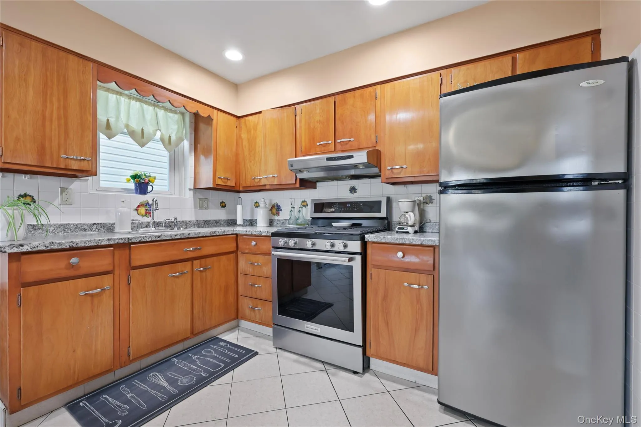 Kitchen featuring stainless steel appliances, brown cabinetry, backsplash, light tile patterned floors, and recessed lighting Kitchen featuring stainless steel appliances, brown cabinetry, backsplash, light tile patterned floors, and recessed lighting