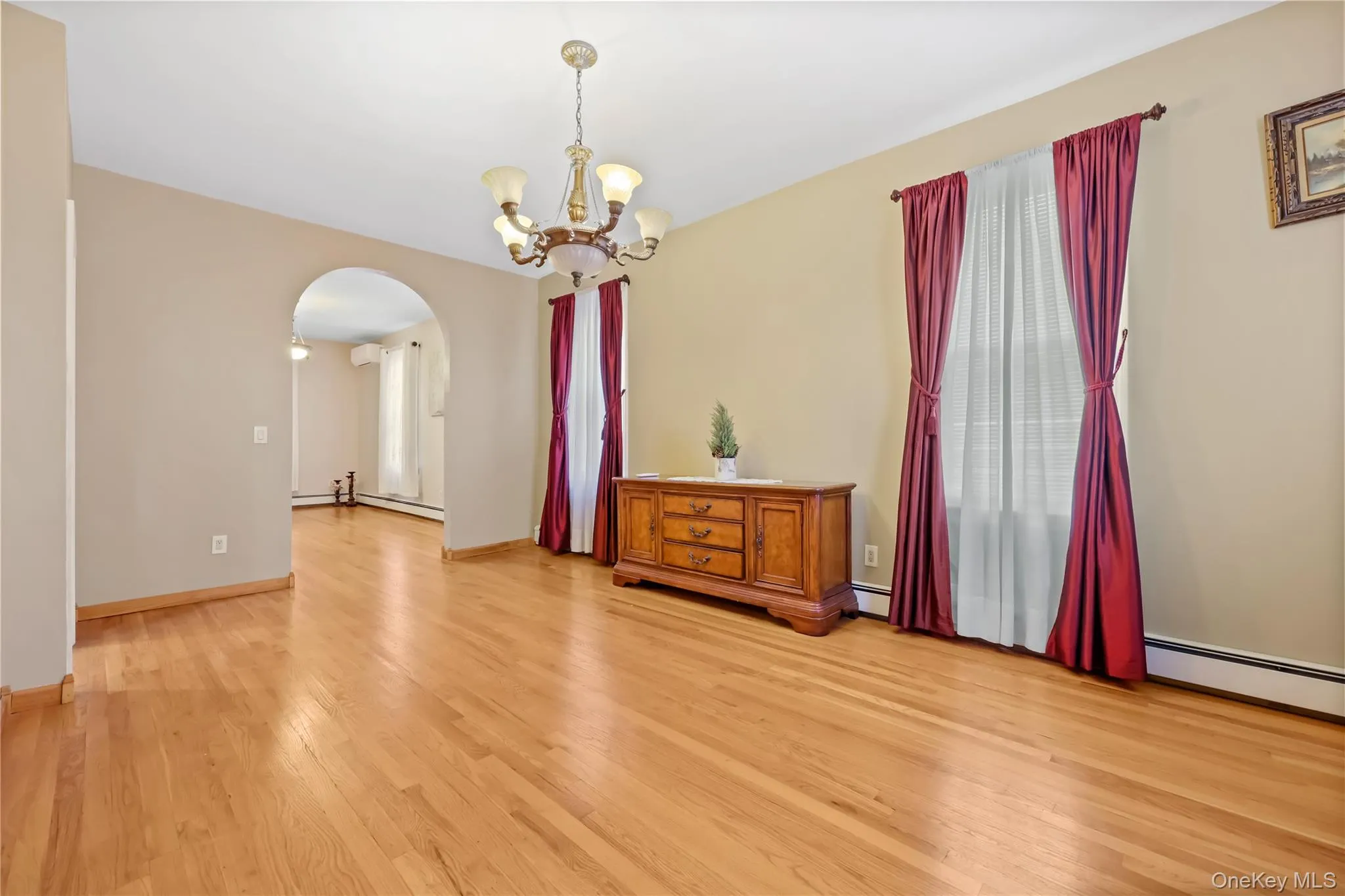 Unfurnished room with arched walkways, a chandelier, light wood-style floors, and a baseboard heating unit Unfurnished room with arched walkways, a chandelier, light wood-style floors, and a baseboard heating unit