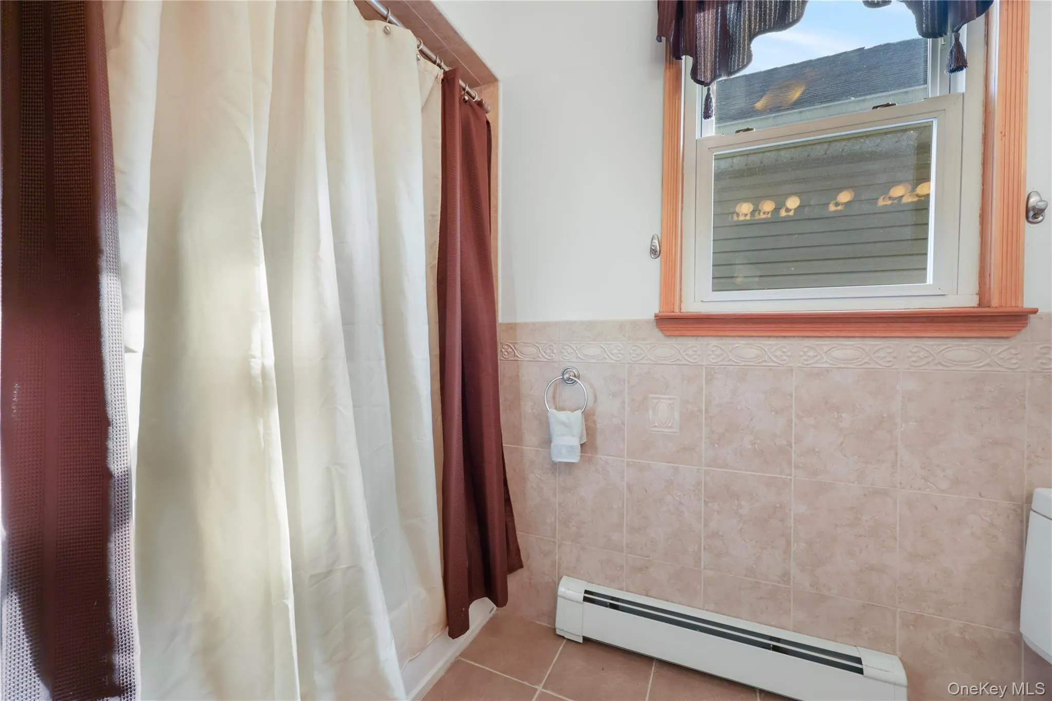 Bathroom featuring baseboard heating, tile patterned flooring, tile walls, and wainscoting Bathroom featuring baseboard heating, tile patterned flooring, tile walls, and wainscoting