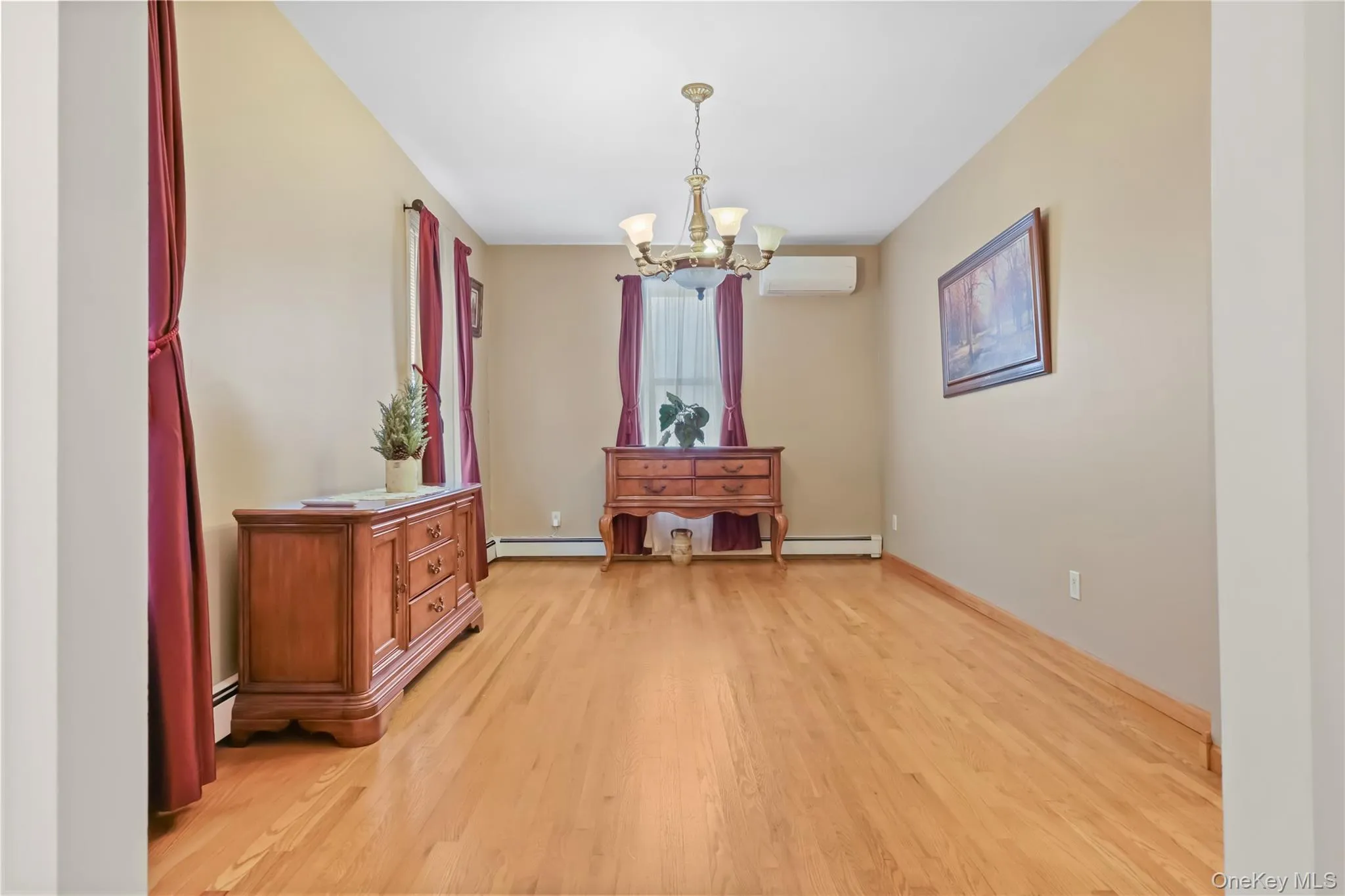 Unfurnished dining area with light wood-style flooring, a chandelier, a wall mounted AC, and a baseboard radiator Unfurnished dining area with light wood-style flooring, a chandelier, a wall mounted AC, and a baseboard radiator