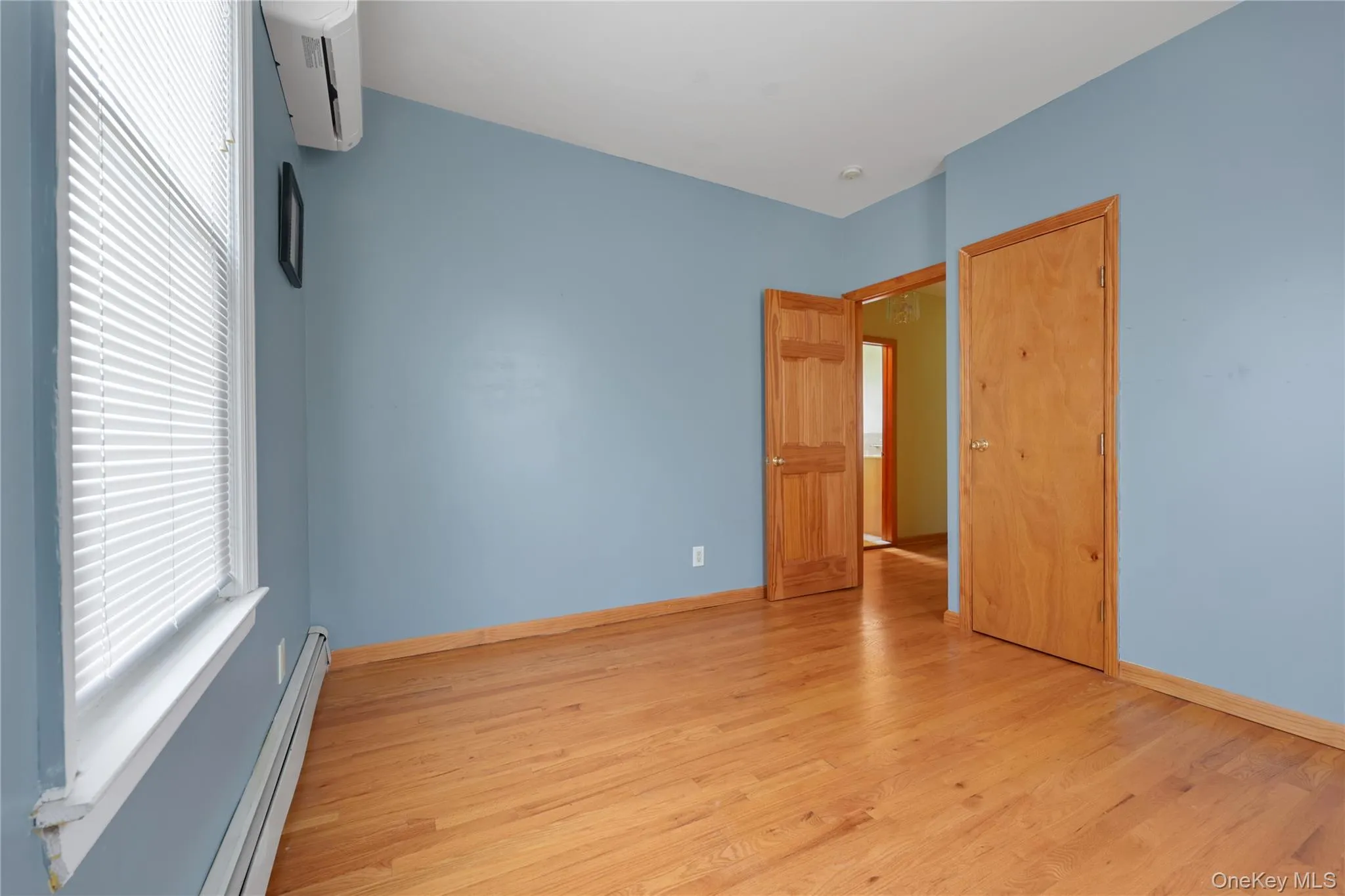 Unfurnished bedroom with a baseboard heating unit, a wall mounted AC, and light wood-style floors Unfurnished bedroom with a baseboard heating unit, a wall mounted AC, and light wood-style floors
