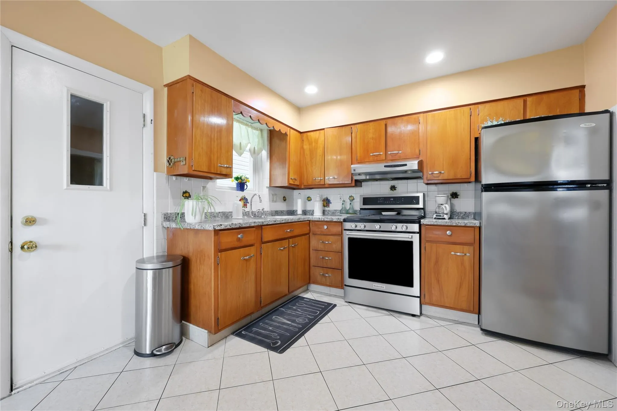 Kitchen with stainless steel appliances, brown cabinetry, decorative backsplash, light tile patterned flooring, and recessed lighting Kitchen with stainless steel appliances, brown cabinetry, decorative backsplash, light tile patterned flooring, and recessed lighting