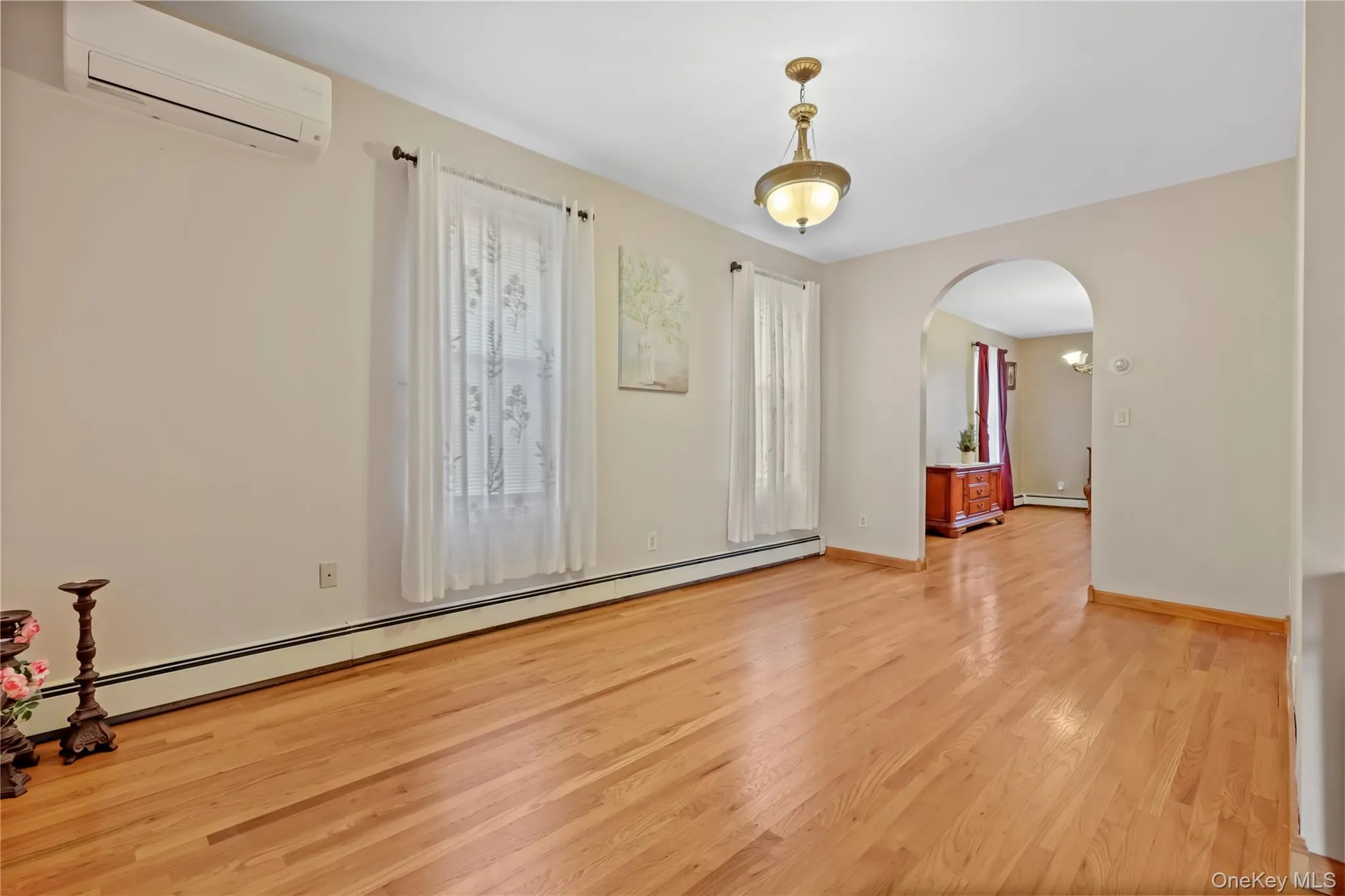 Foyer with baseboard heating, arched walkways, light wood finished floors, and a wall mounted air conditioner Foyer with baseboard heating, arched walkways, light wood finished floors, and a wall mounted air conditioner