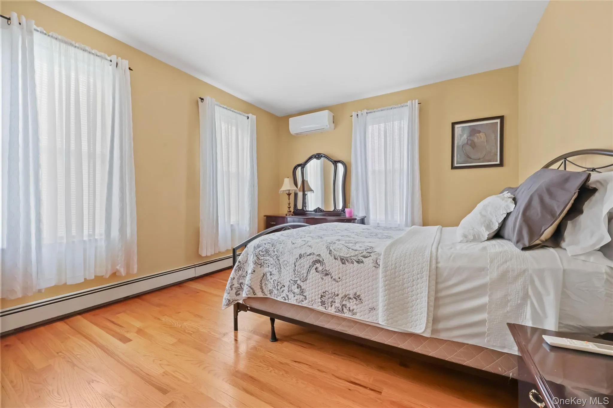 Bedroom featuring a baseboard radiator, light wood finished floors, and a wall unit AC Bedroom featuring a baseboard radiator, light wood finished floors, and a wall unit AC