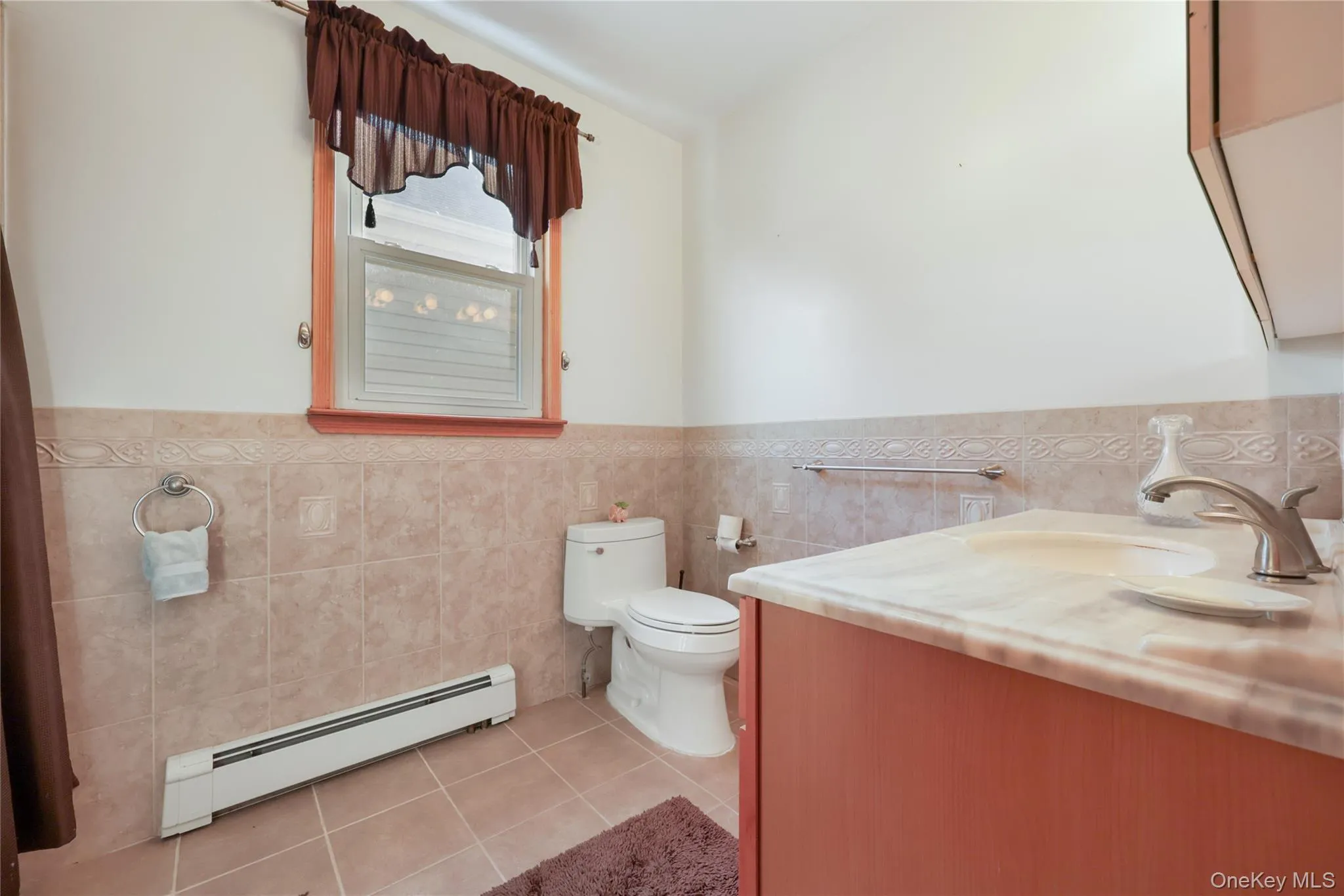 Bathroom with light tile patterned floors, a baseboard radiator, tile walls, a wainscoted wall, and vanity Bathroom with light tile patterned floors, a baseboard radiator, tile walls, a wainscoted wall, and vanity