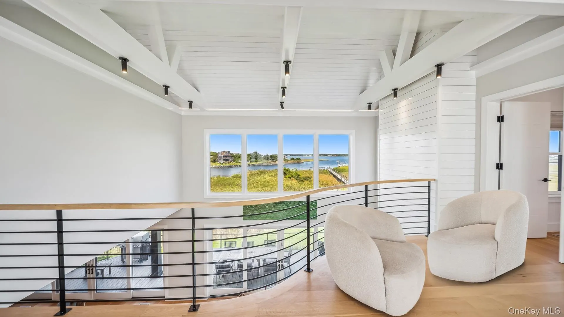Corridor featuring an upstairs landing, beam ceiling, wood finished floors, a water view, and high vaulted ceiling Corridor featuring an upstairs landing, beam ceiling, wood finished floors, a water view, and high vaulted ceiling