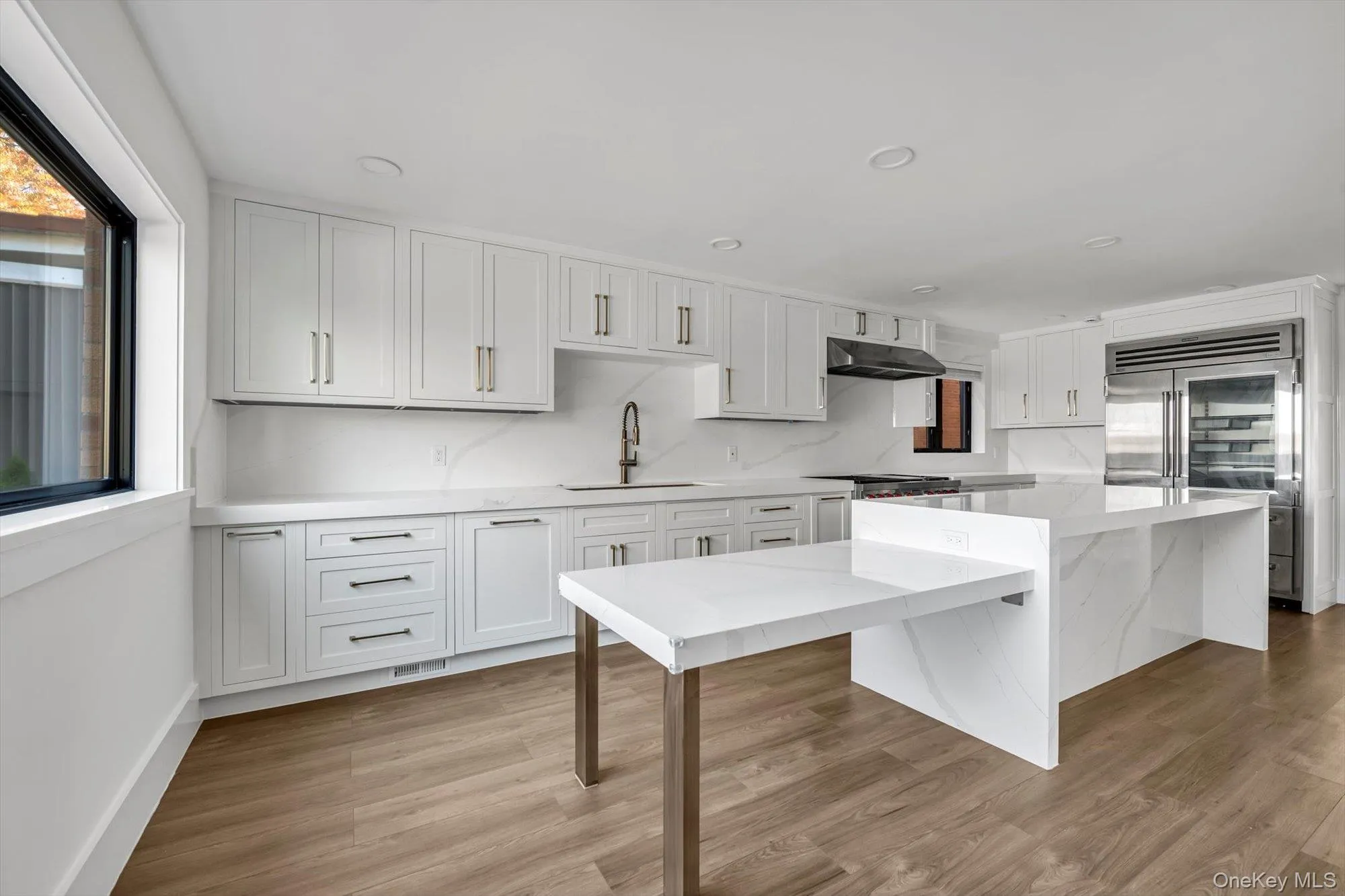 Kitchen featuring white cabinets, light wood-style floors, stainless steel built in fridge, a breakfast bar, and light stone counters Kitchen featuring white cabinets, light wood-style floors, stainless steel built in fridge, a breakfast bar, and light stone counters